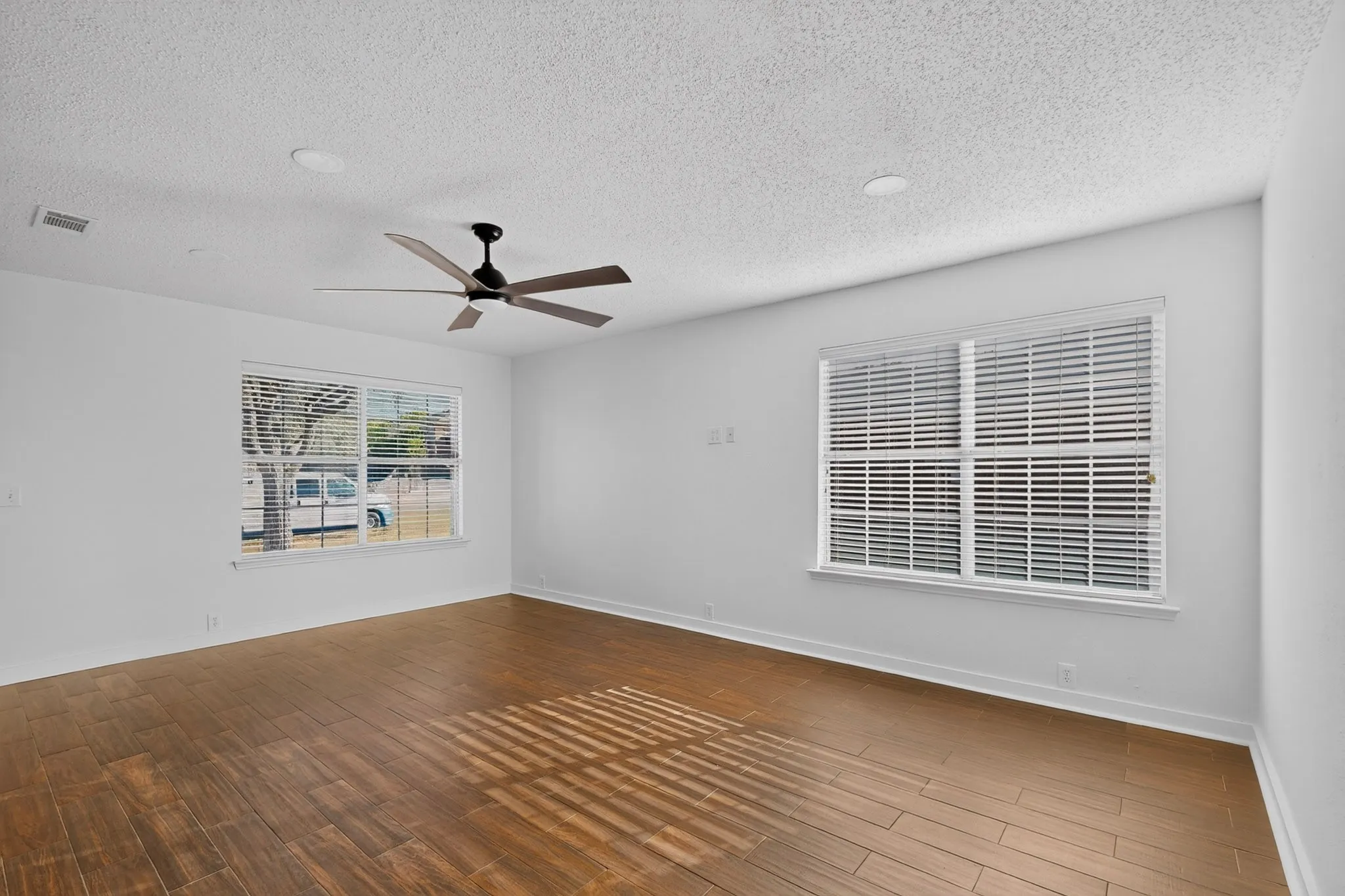 Spacious room featuring wood-finish flooring, white walls, and a ceiling fan