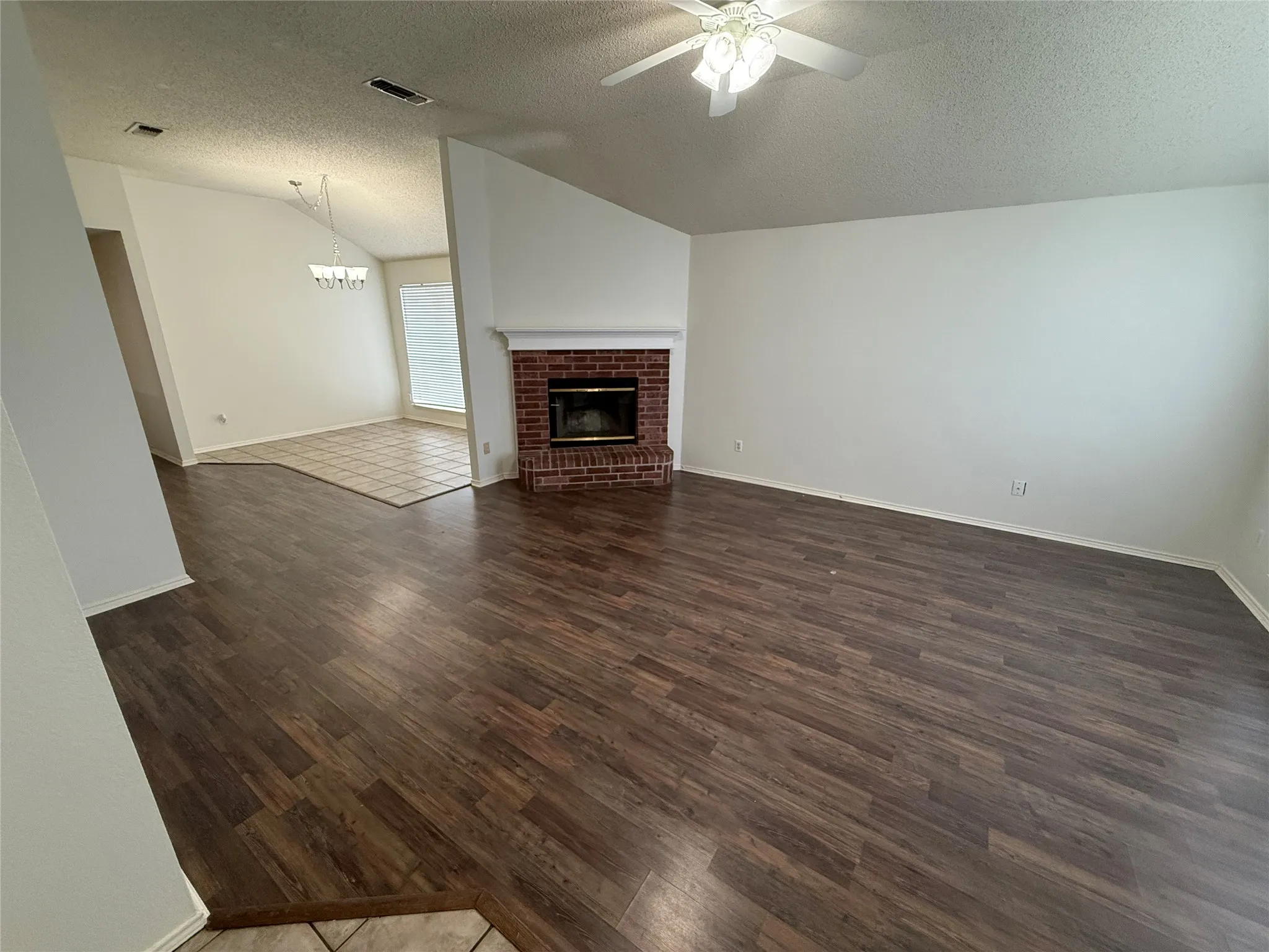 Spacious room featuring wood-finish flooring, a brick fireplace, and a ceiling fan