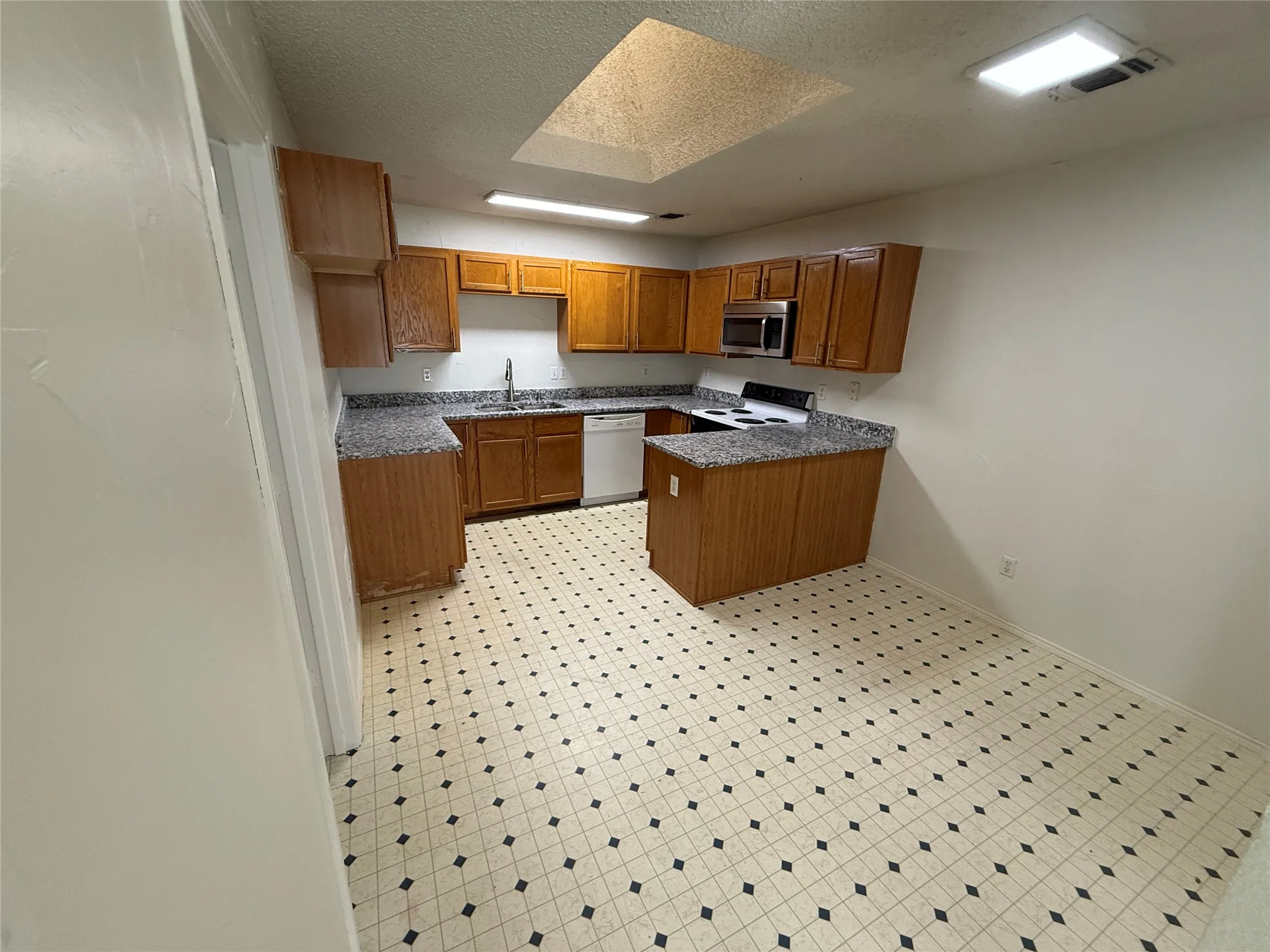 U-shaped kitchen with wood-finish cabinetry, light-toned countertops, and checkerboard pattern flooring