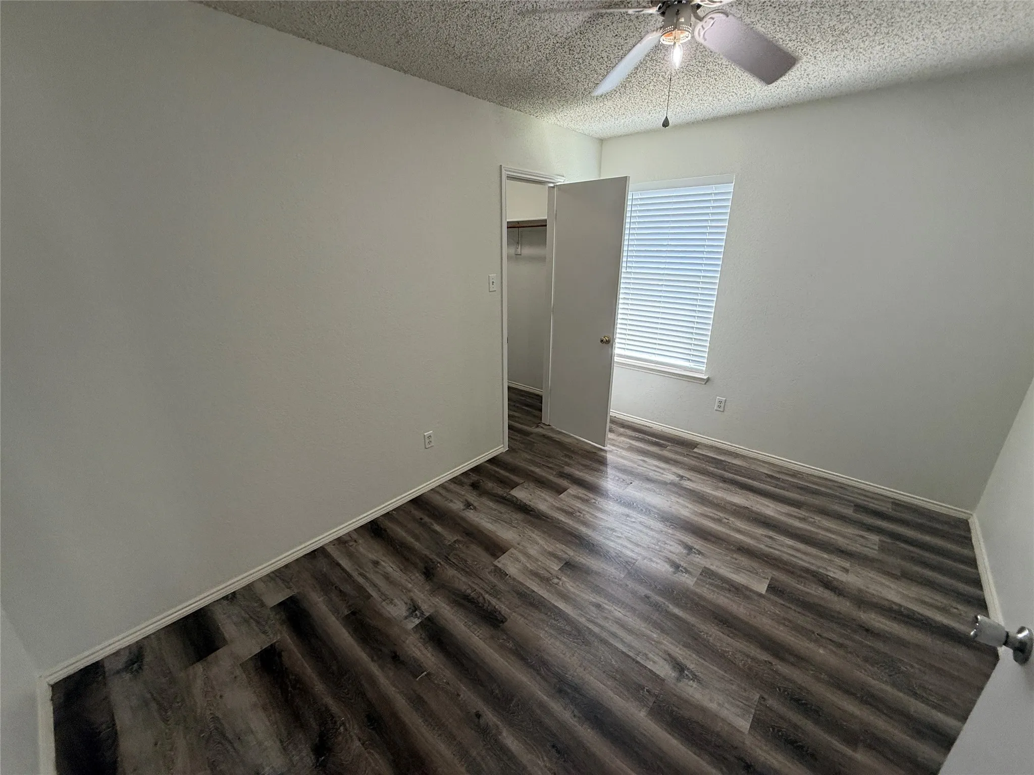 Wood-finish flooring, ceiling fan with integrated lighting, window with blinds, and a built-in closet with shelving
