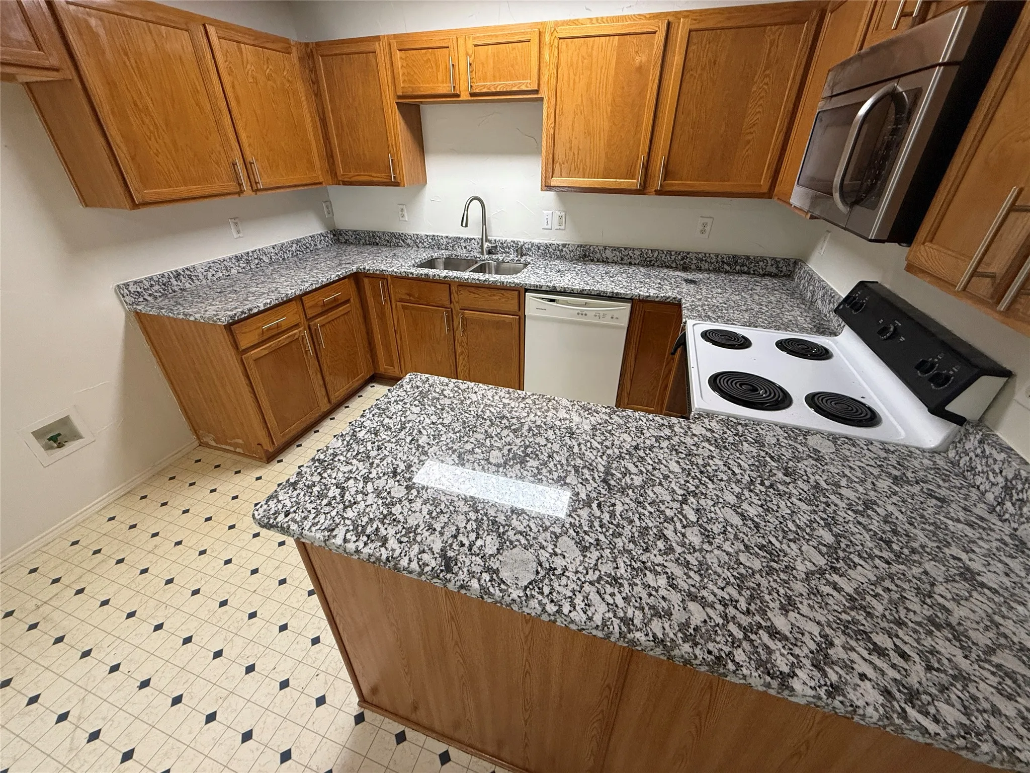Kitchen featuring wood cabinetry, granite-look countertops, stainless steel microwave, and white appliances