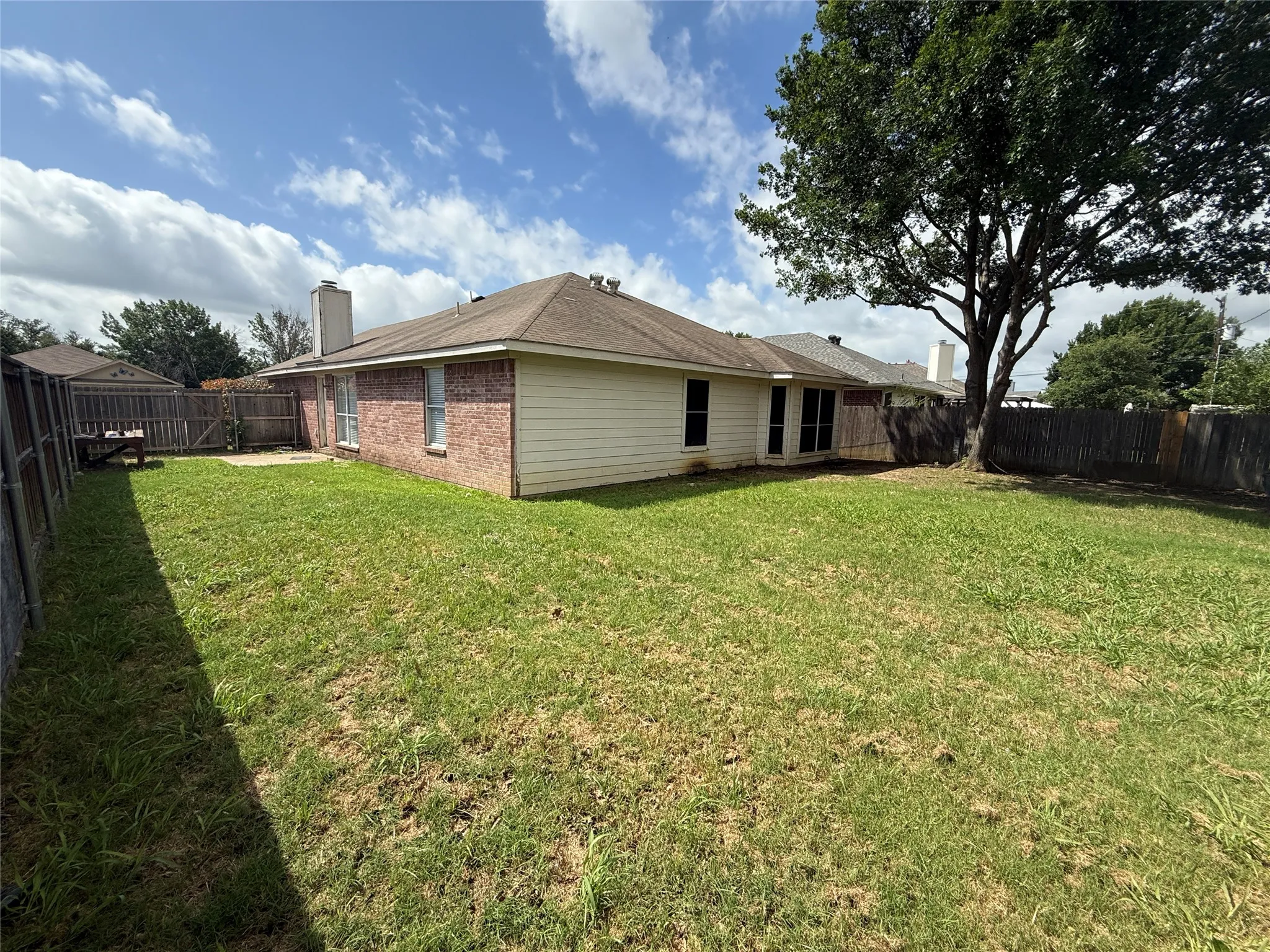 Expansive grassy yard with a mature tree, privacy fencing, brick exterior, and a visible chimney