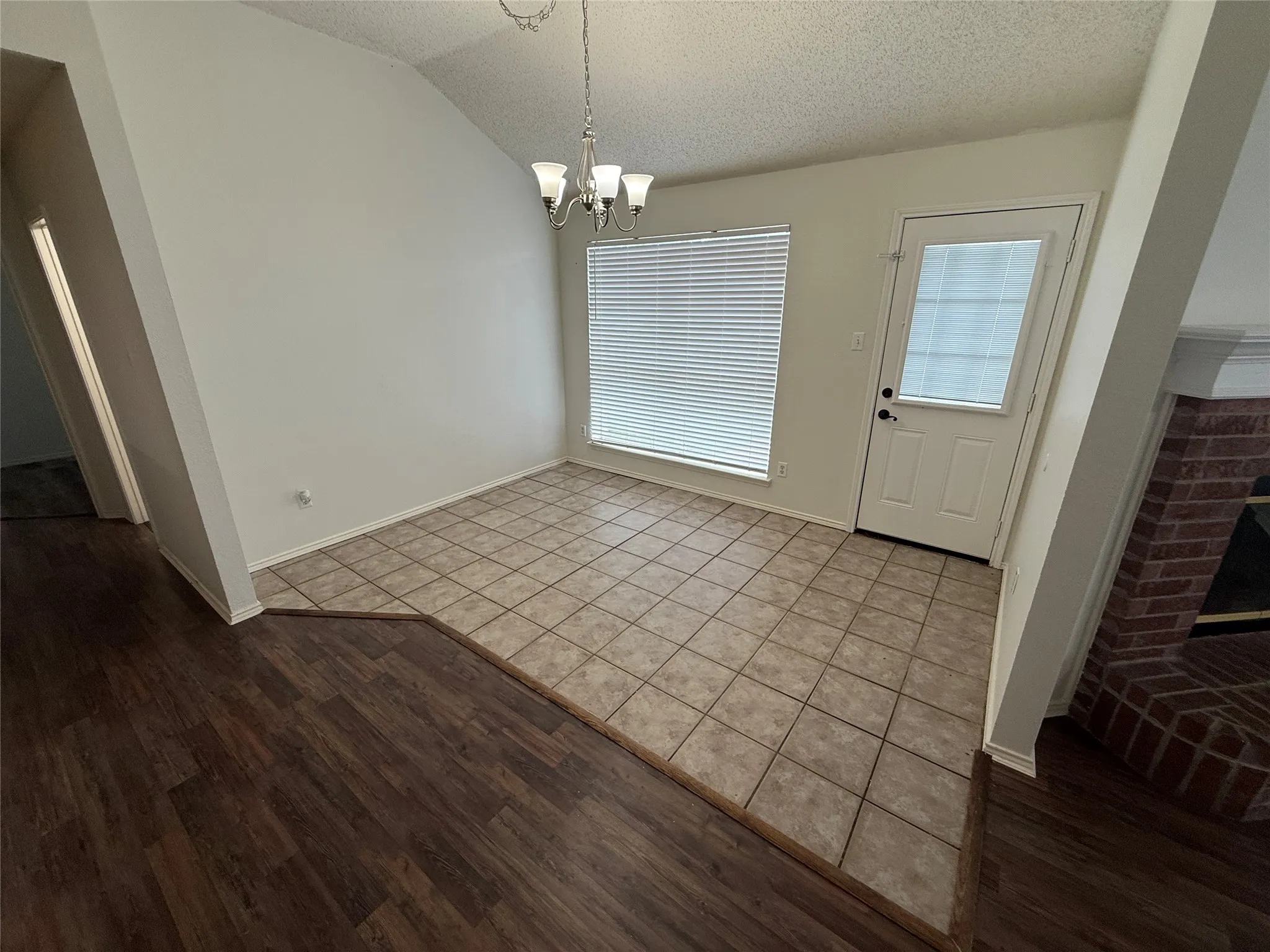 Vaulted ceiling with a chandelier, tile flooring, wood-finish flooring, and a white paneled door with window insert