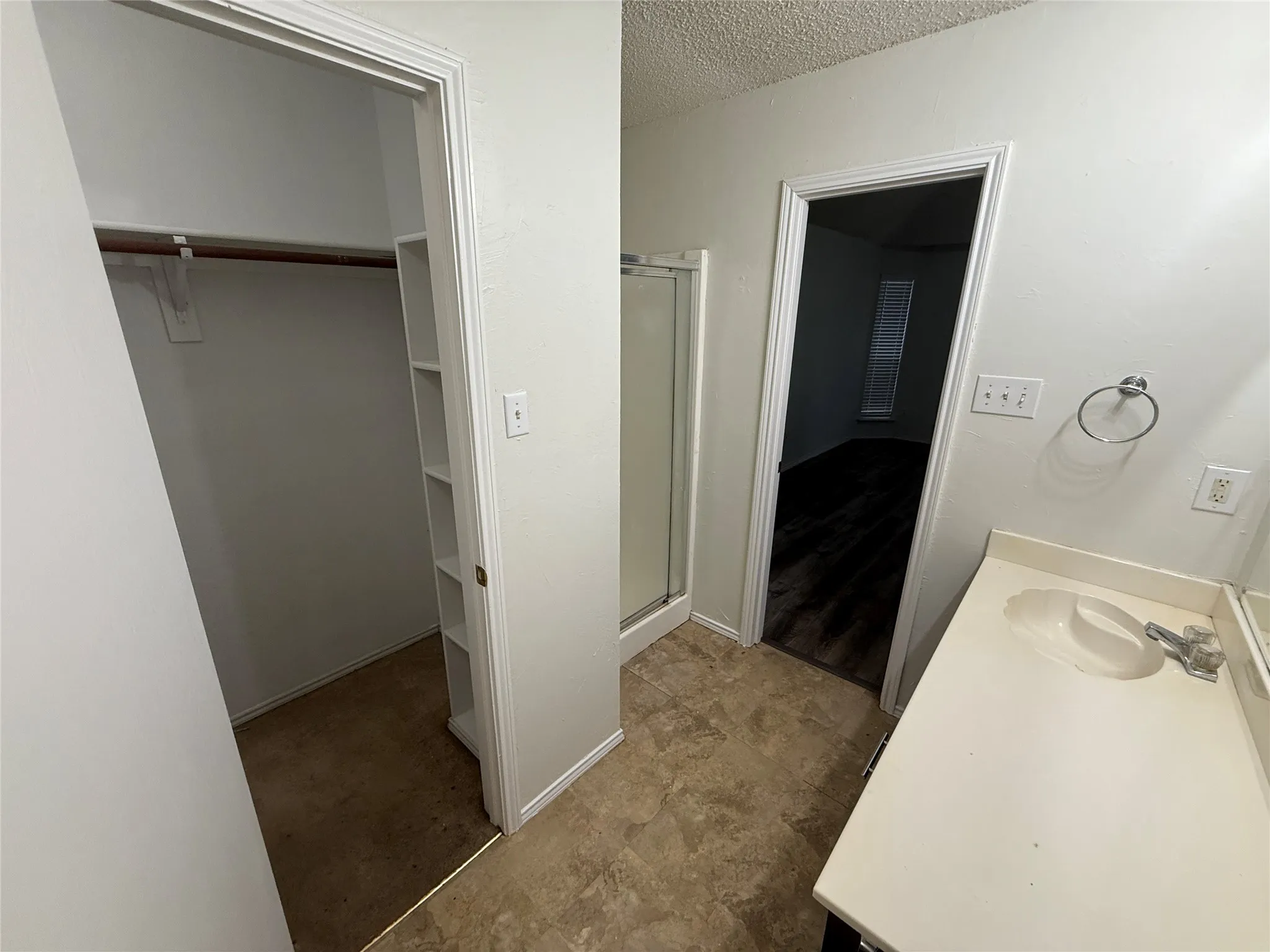 Built-in shelving, shower enclosure, single vanity, and wood-finish flooring visible through doorway