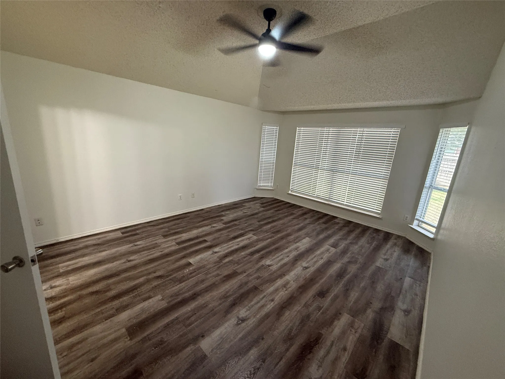 Vaulted ceiling with a ceiling fan, wood-finish flooring, and multiple windows with blinds