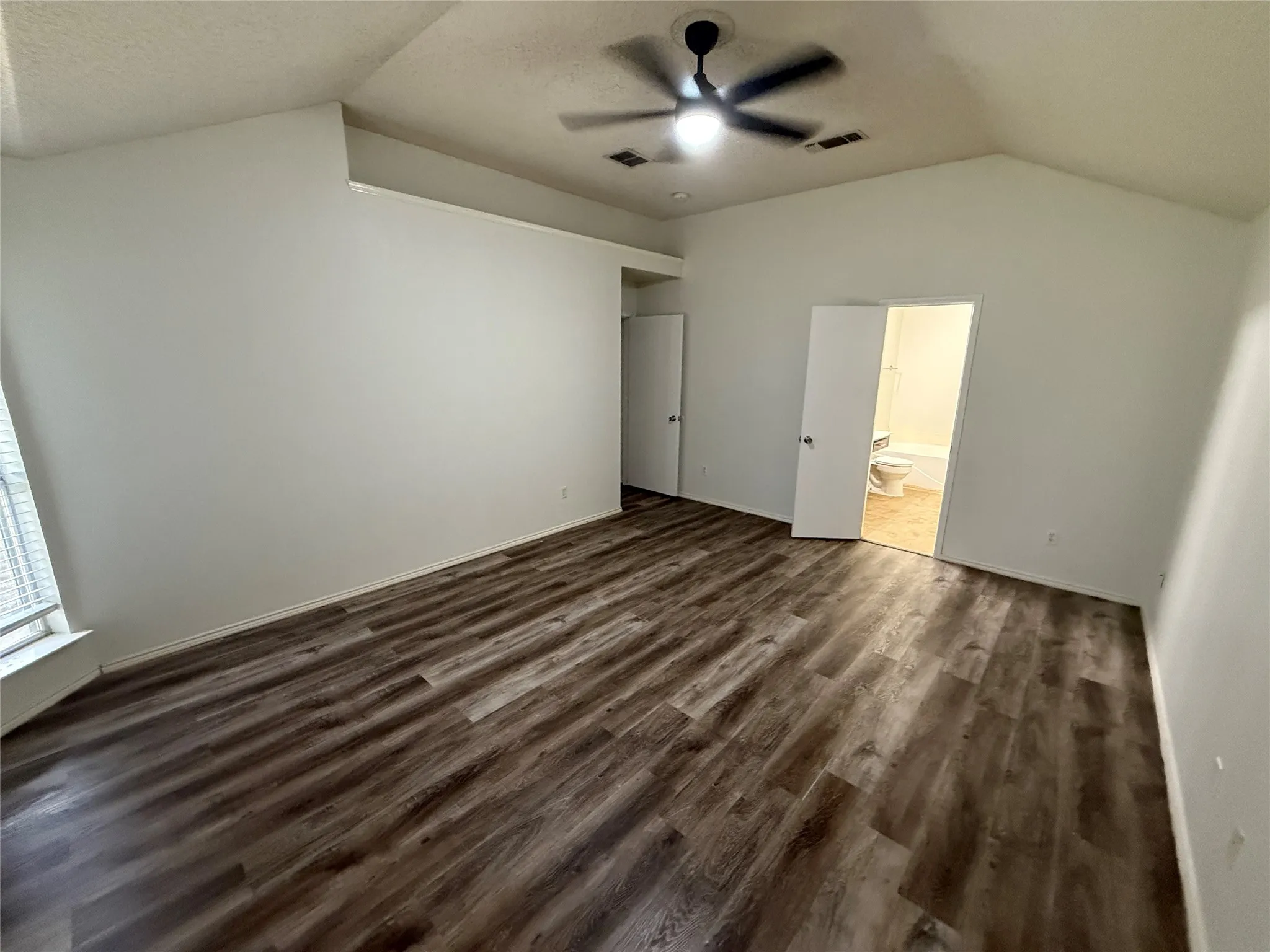 Vaulted ceiling with an attached ceiling fan, wood-finish flooring, and white interior doors