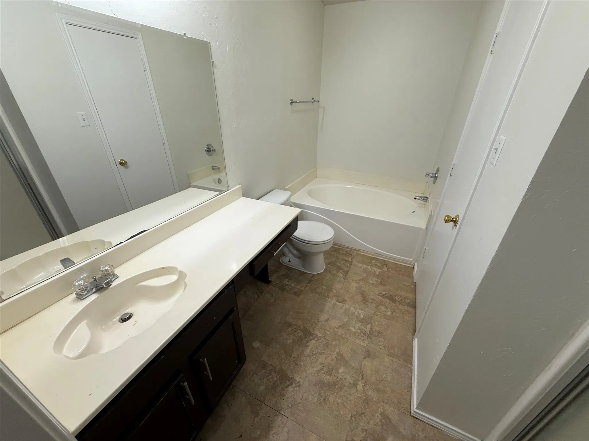 Bathroom featuring a single vanity with an integrated sink, full-width mirror, wood-finish cabinetry, and a built-in bathtub with shower