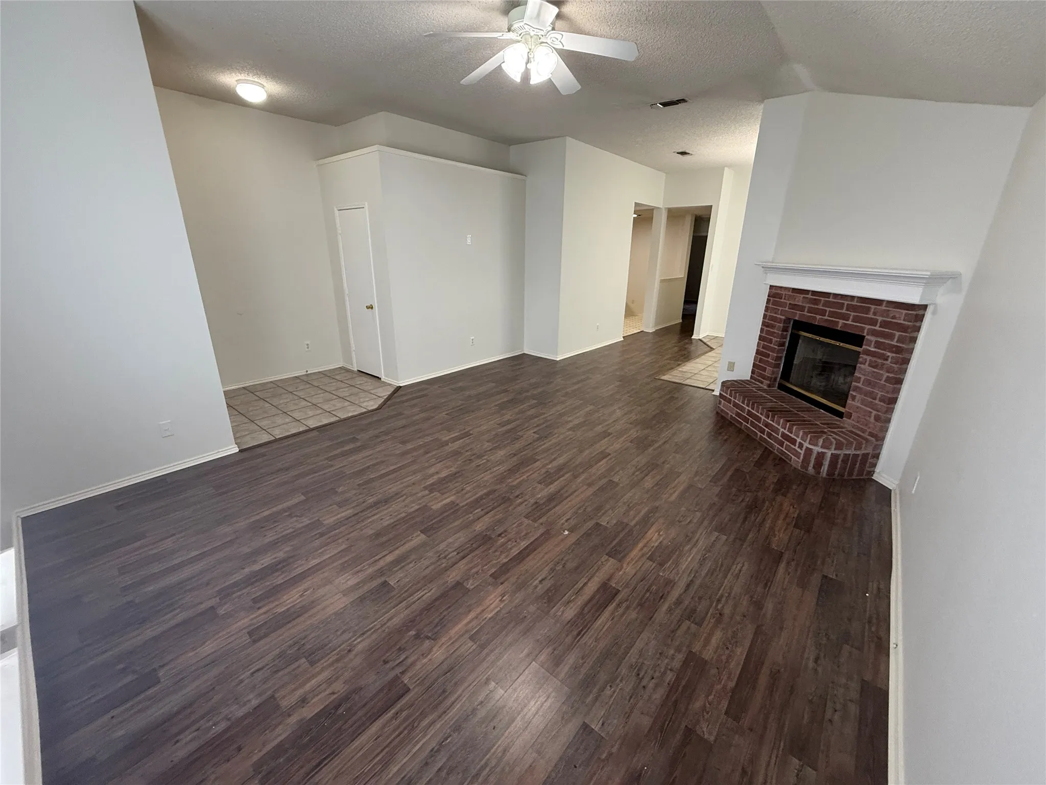 Wood-finish flooring, brick fireplace with a white mantel, ceiling fan, and recessed lighting
