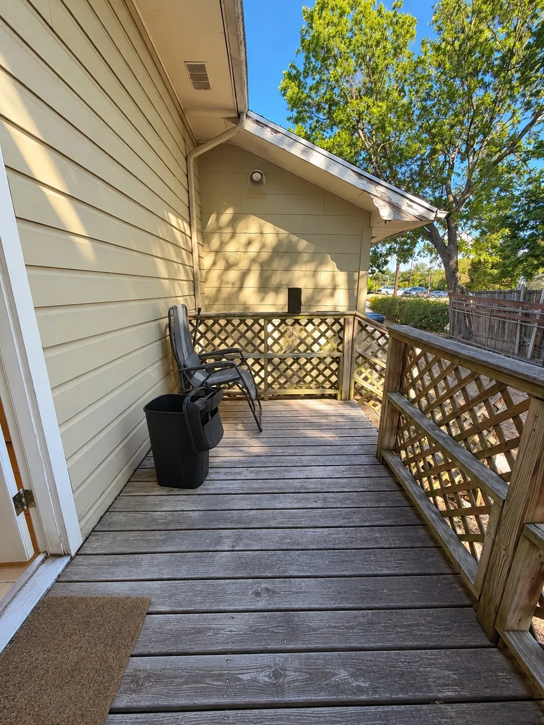 Wood plank decking with lattice railing, horizontal siding, and an exterior wall light