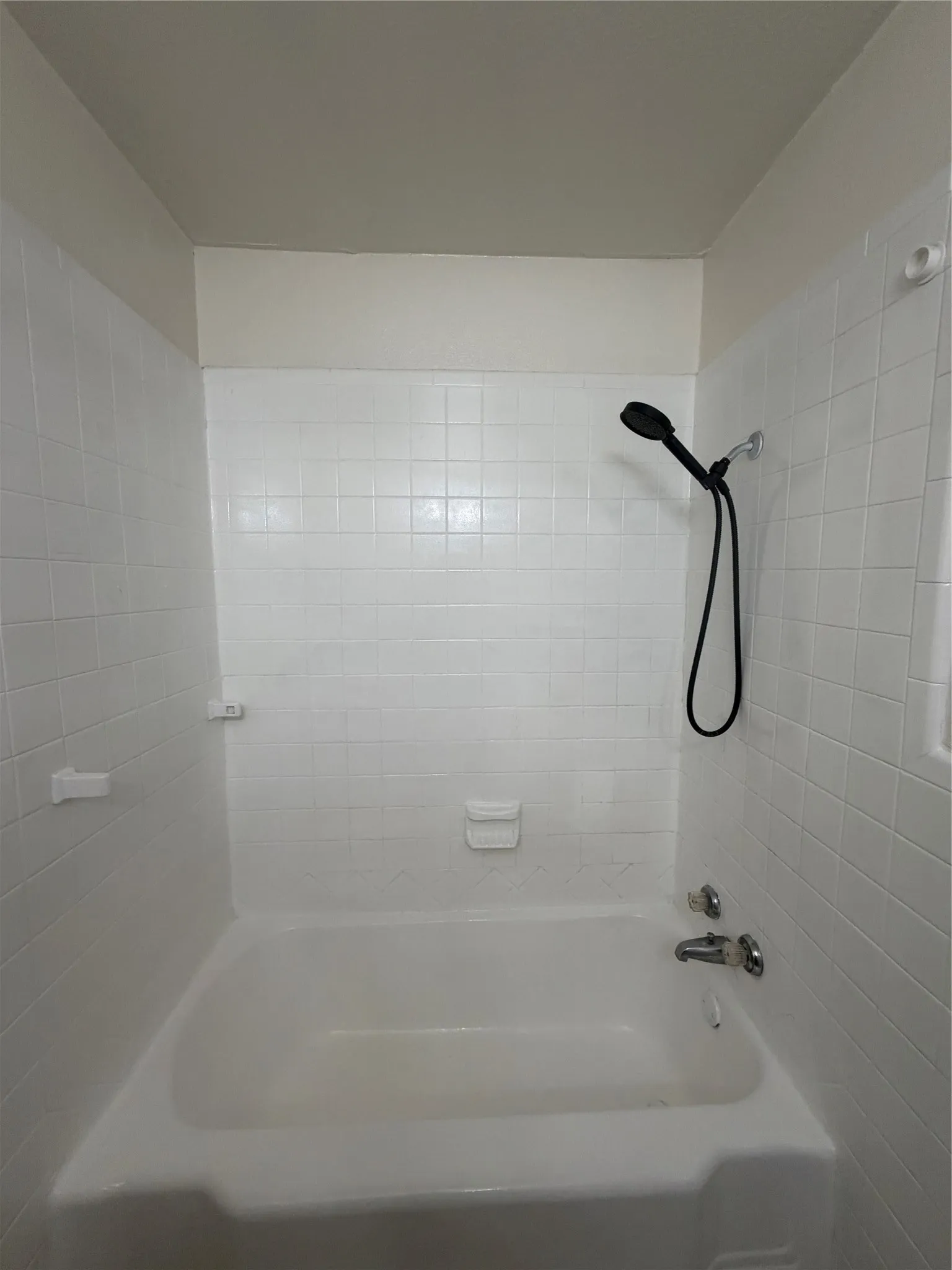 White tiled shower surround with a built-in bathtub and a handheld shower fixture