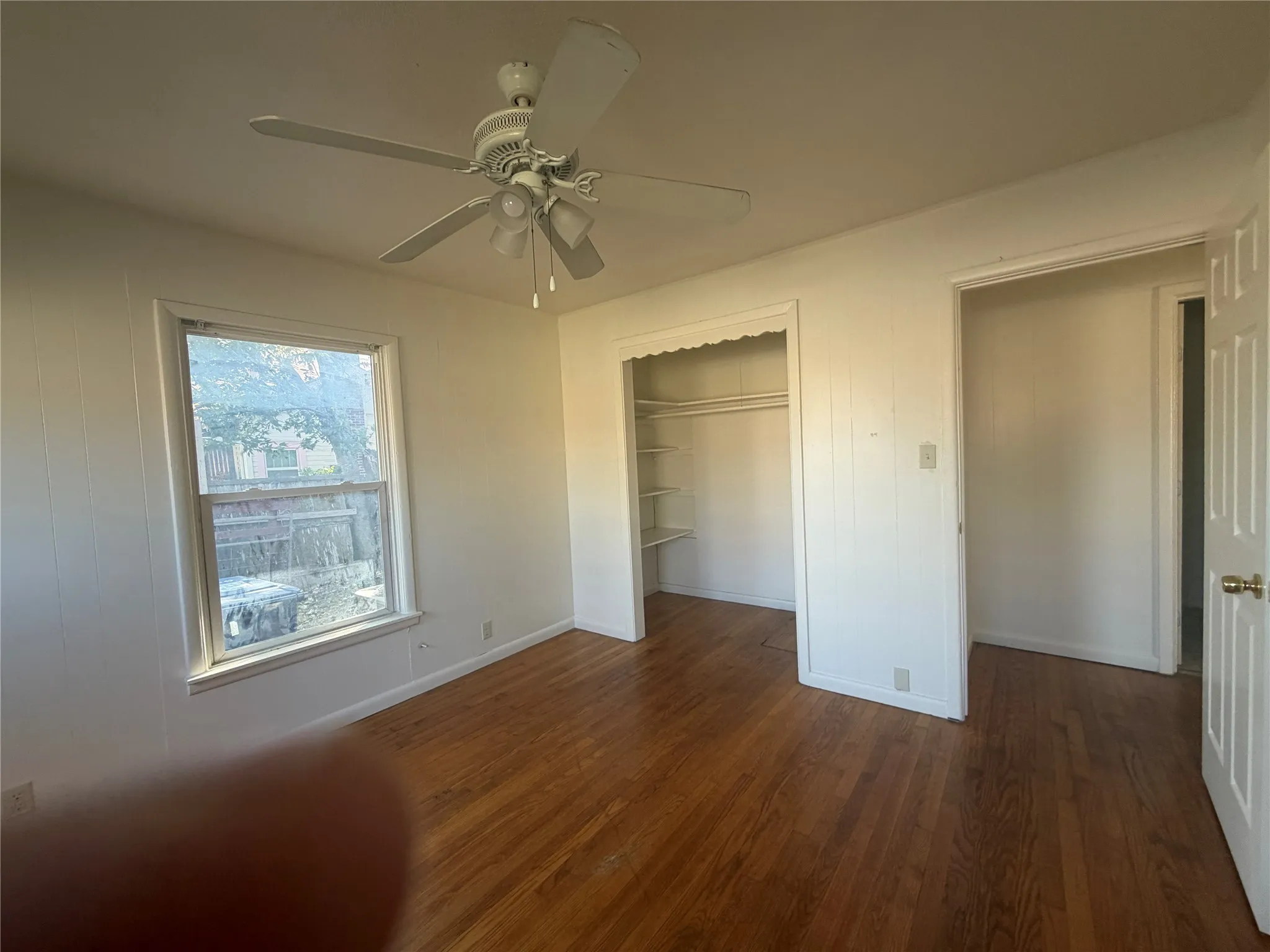 Wood-finish flooring, ceiling fan with integrated lighting, a double-hung window, and a built-in closet with shelving