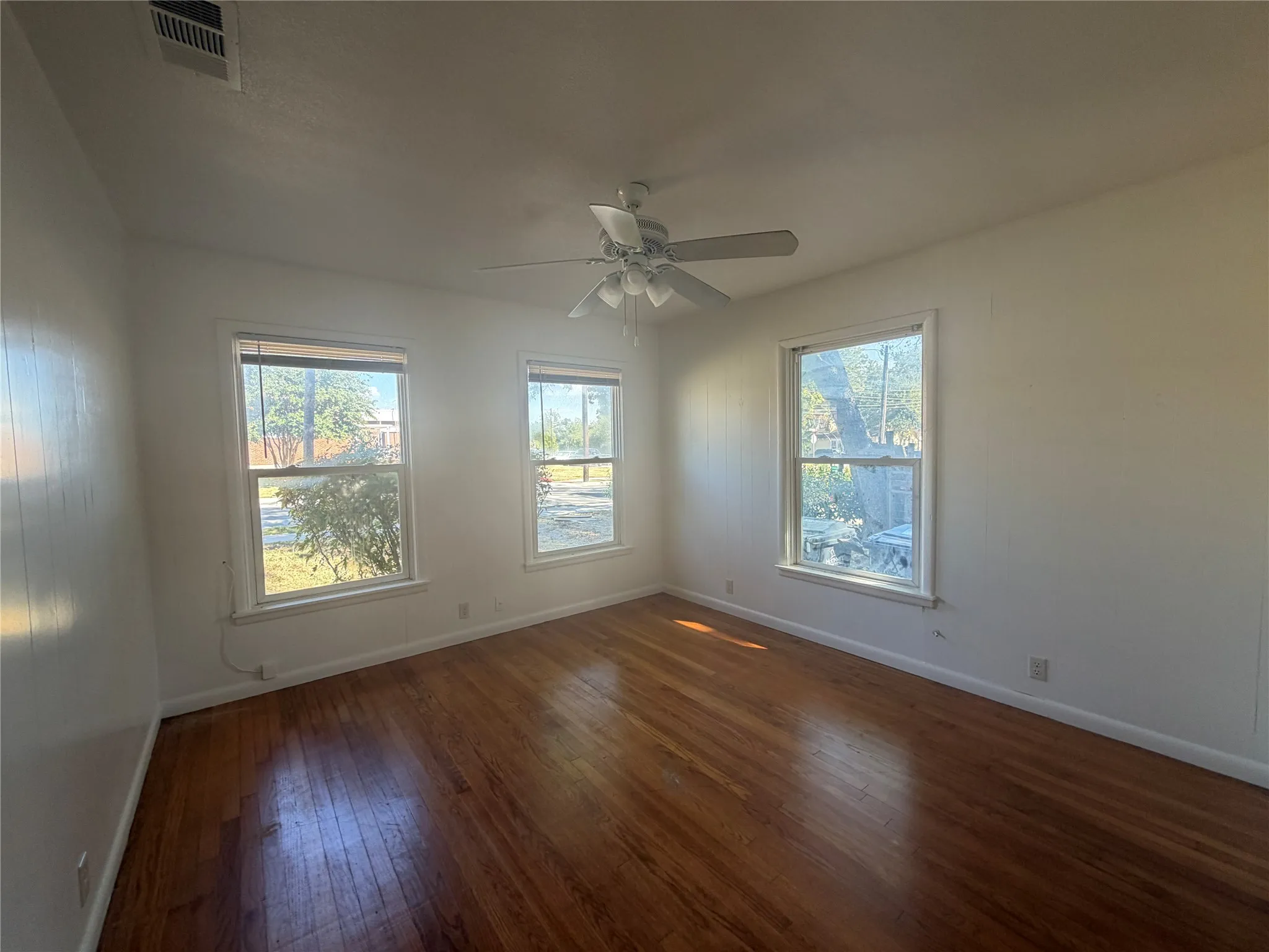 Hardwood flooring, white walls, three windows, ceiling fan with integrated lighting