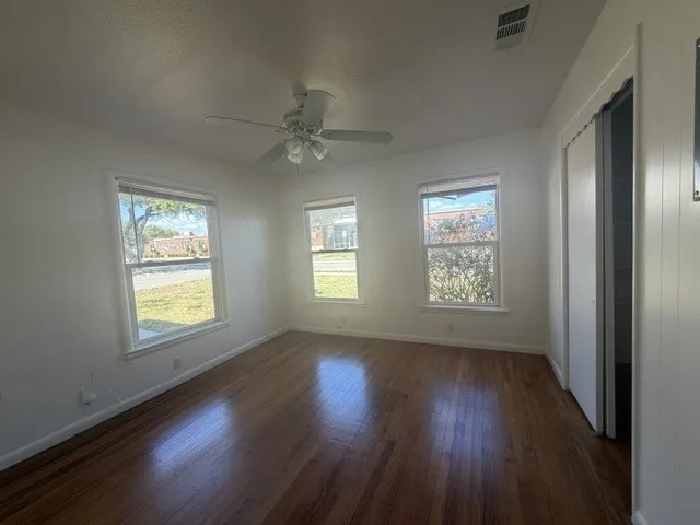 Wood-finish flooring throughout, white walls, multiple windows, ceiling fan, and a built-in closet with bi-fold doors