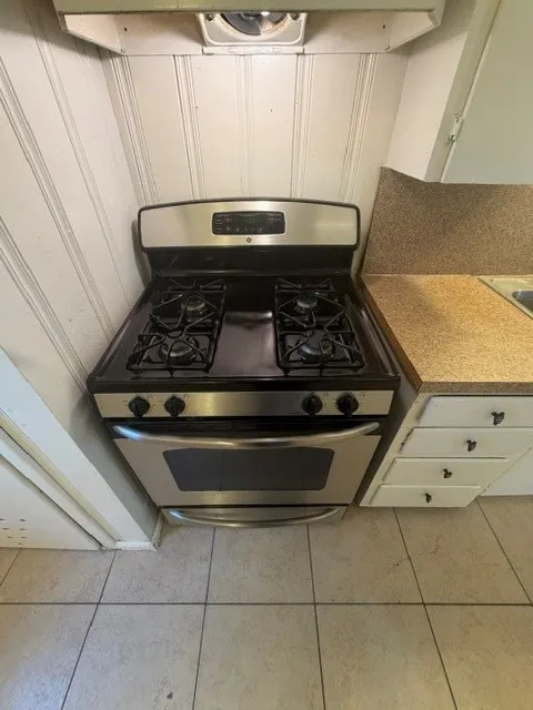 Stainless steel gas range with four burners, integrated oven, and overhead exhaust fan