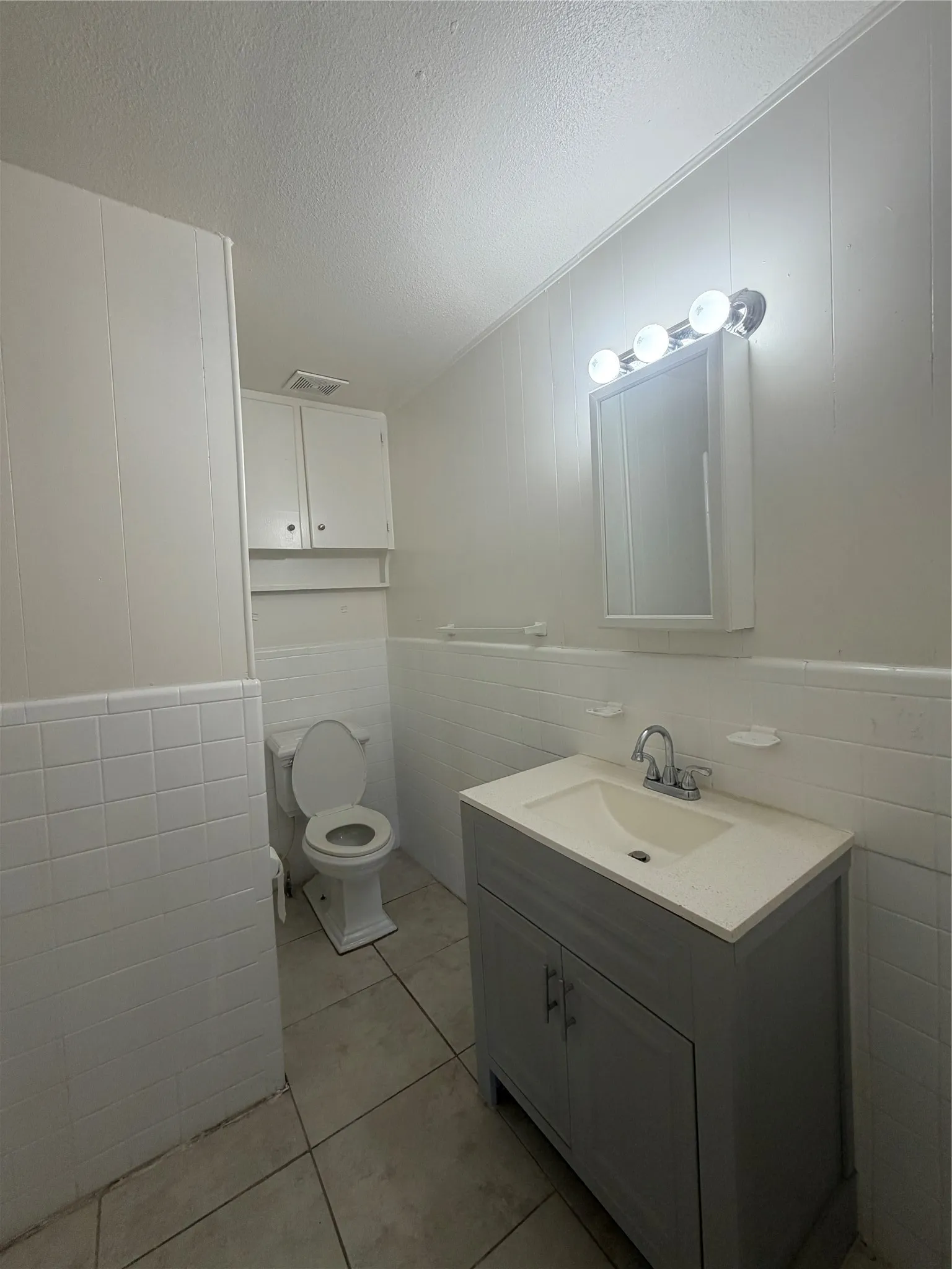 Bathroom featuring a gray vanity with an integrated sink, tiled flooring, white tiled wainscoting, and an overhead light fixture