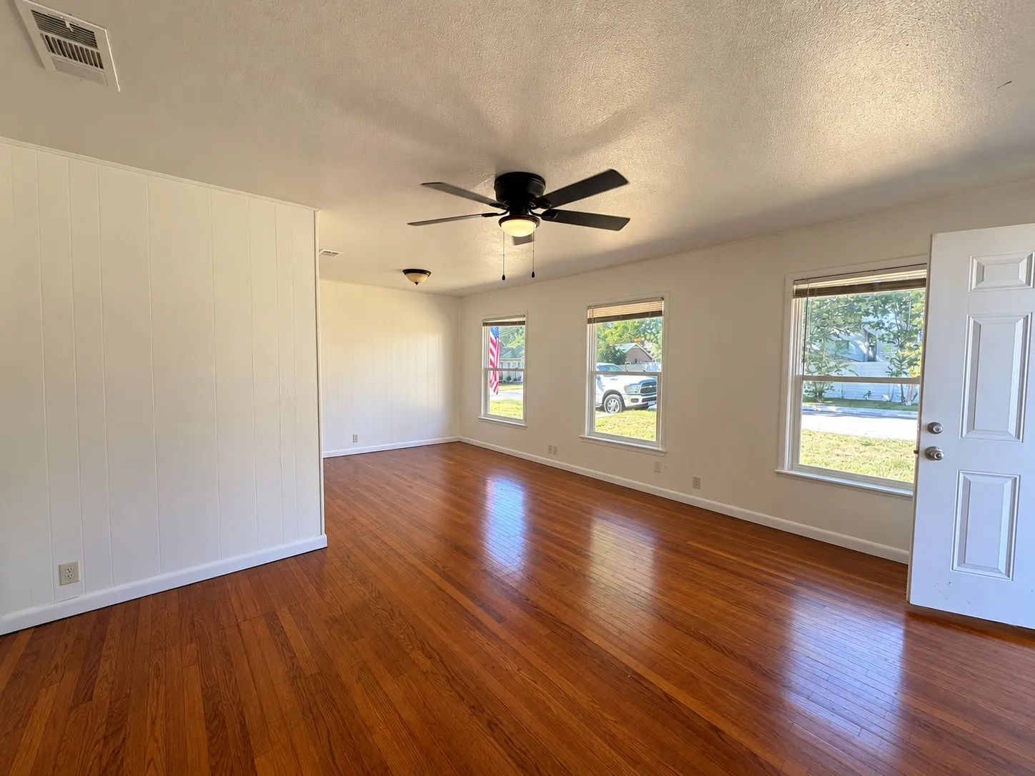 Hardwood-style flooring throughout, white vertical paneling, white door, and multiple windows