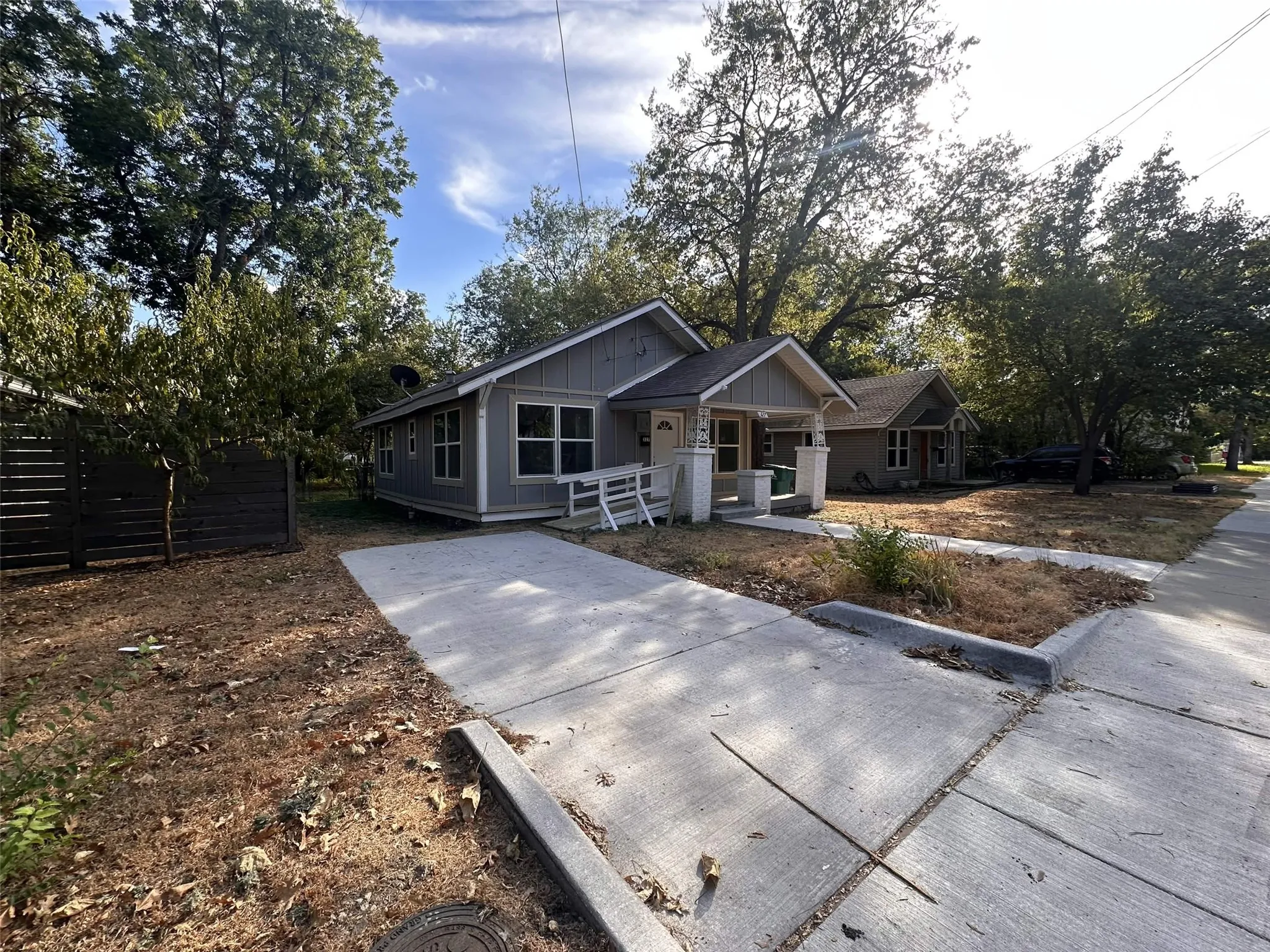 Light gray siding with white trim, covered front porch, concrete driveway, concrete walkway, and mature trees