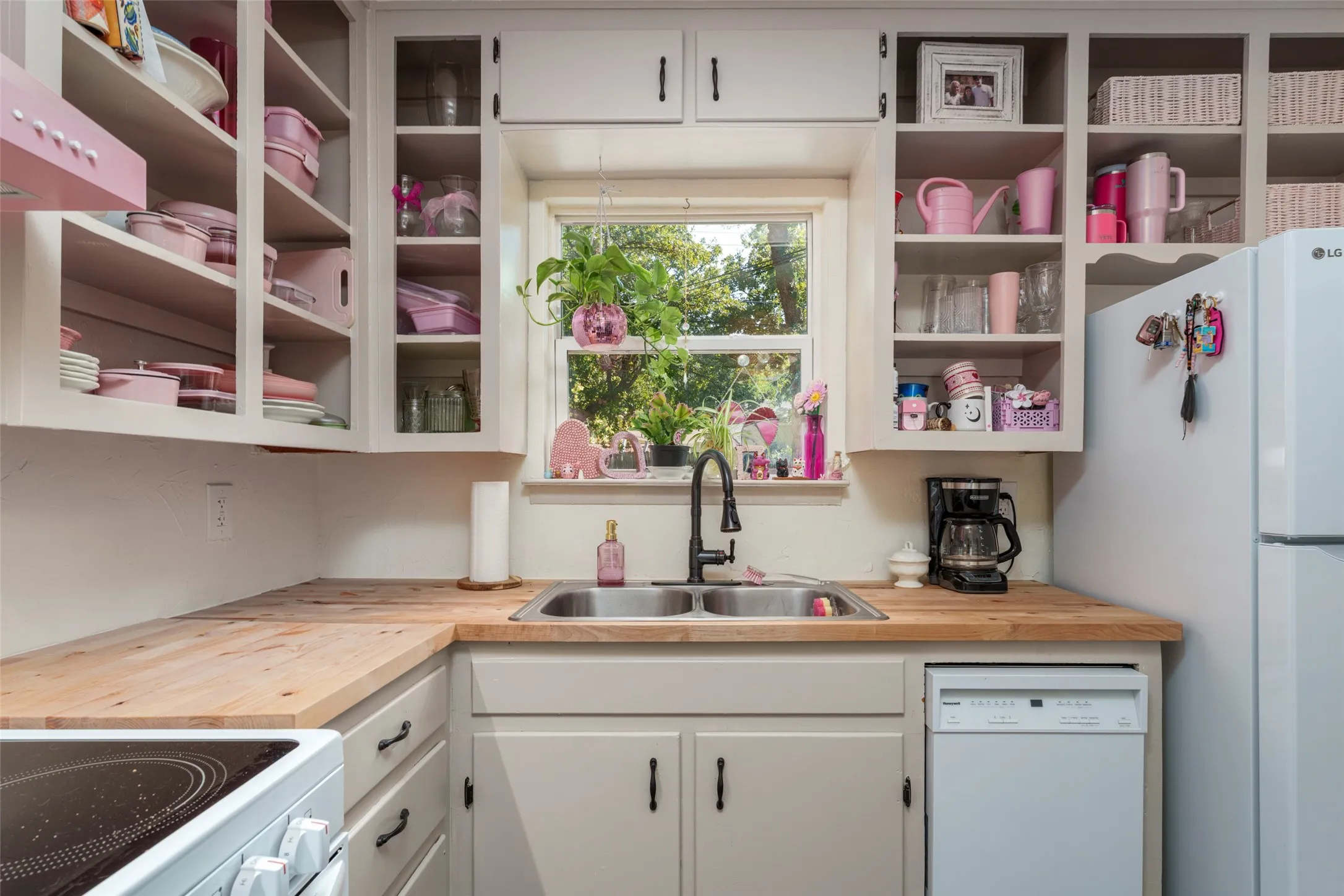 Wood-finish countertops, stainless steel sink, black gooseneck faucet, white cabinetry, and a window with natural light