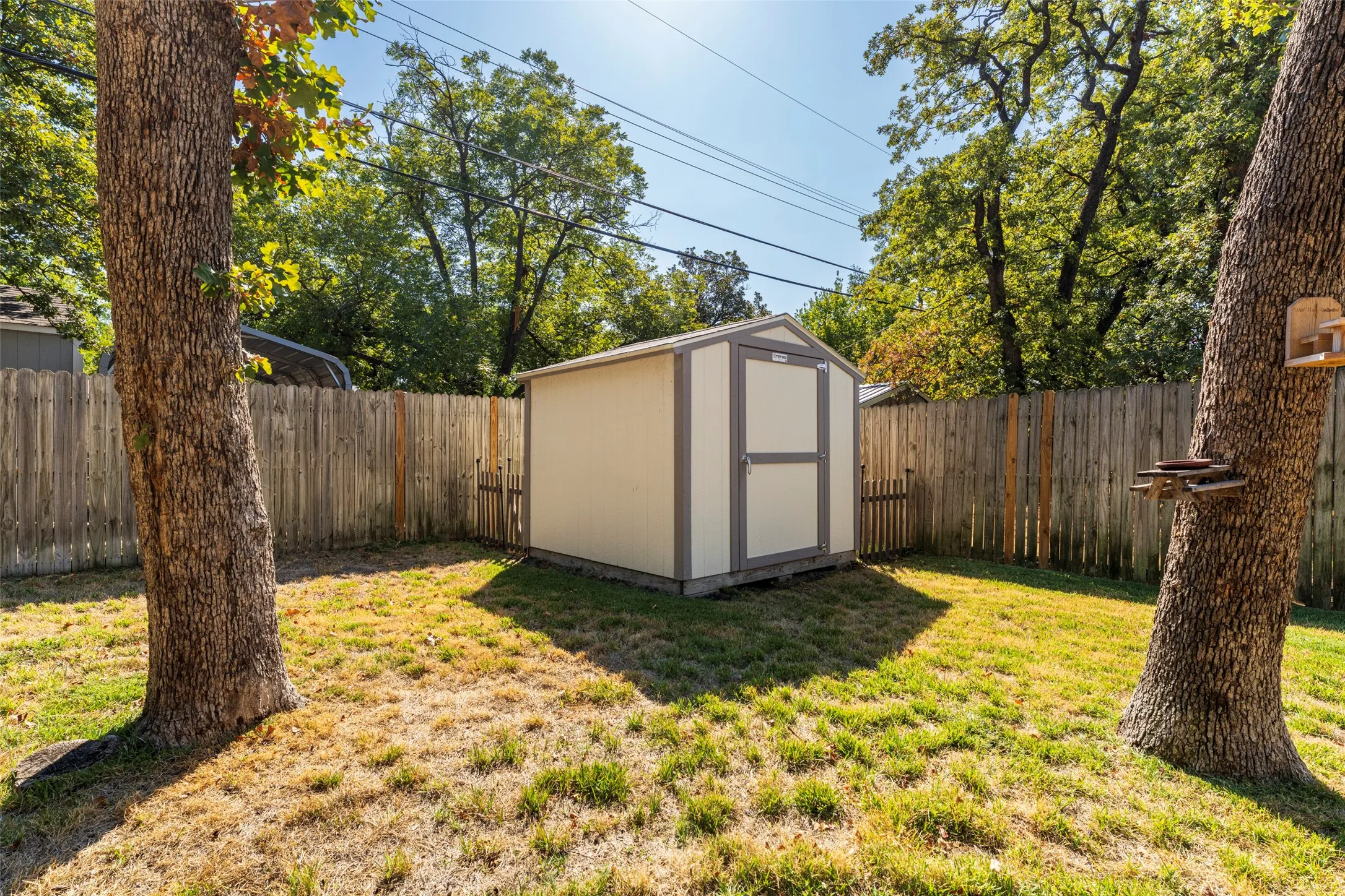 Fenced backyard featuring a storage shed, established trees, and a wooden privacy fence