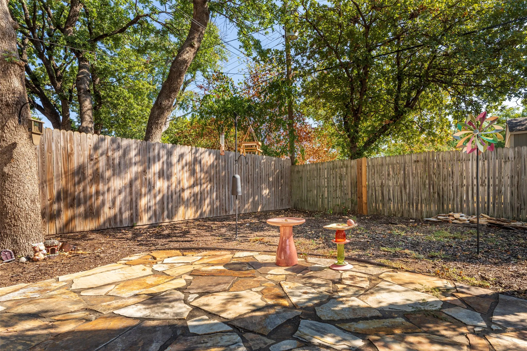 Stone patio with natural flagstone pavers, surrounded by a wood fence, mature trees, and a ground cover of mulch