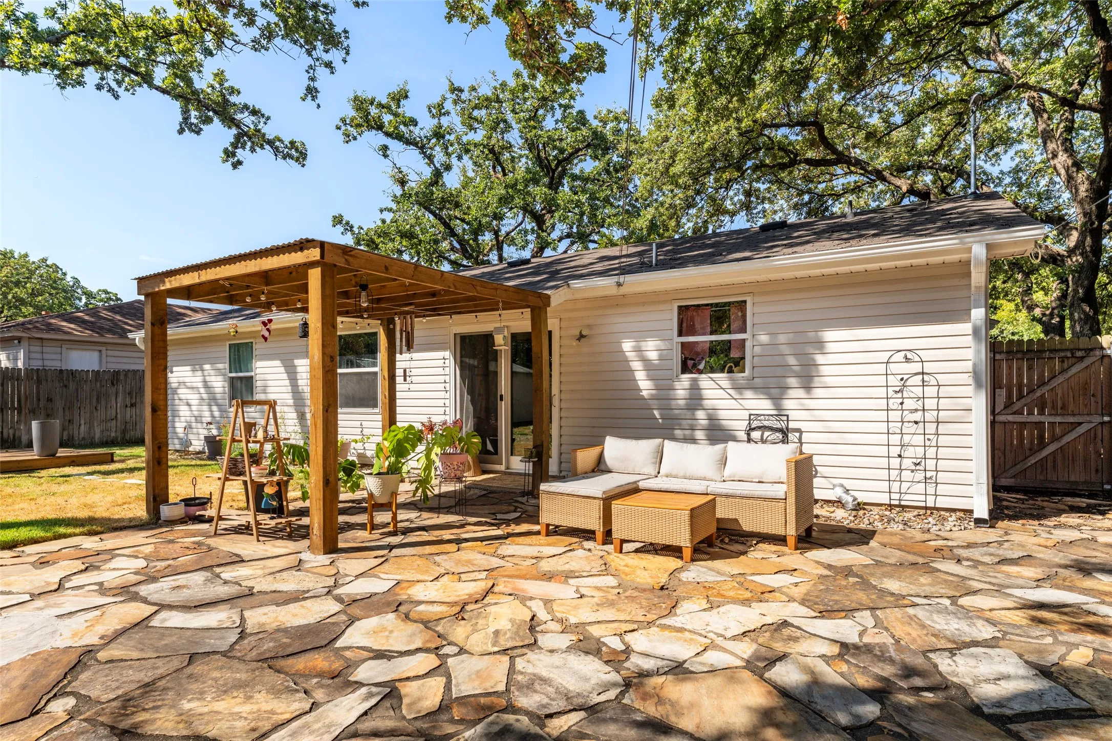 Expansive flagstone patio featuring a wood pergola with a corrugated roof, and a privacy fence