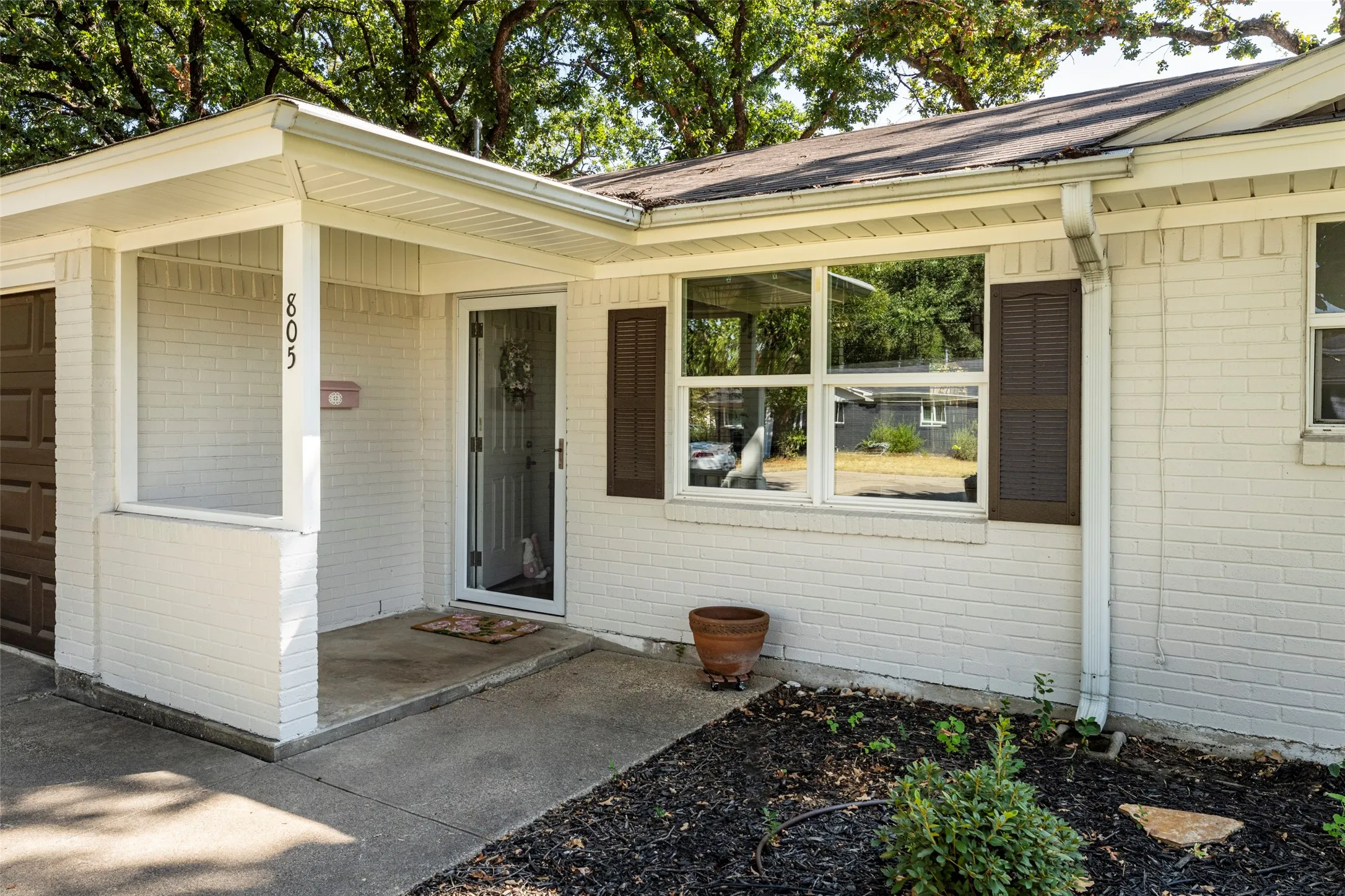 White painted brick exterior with dark shutters, covered entry, and a brown garage door