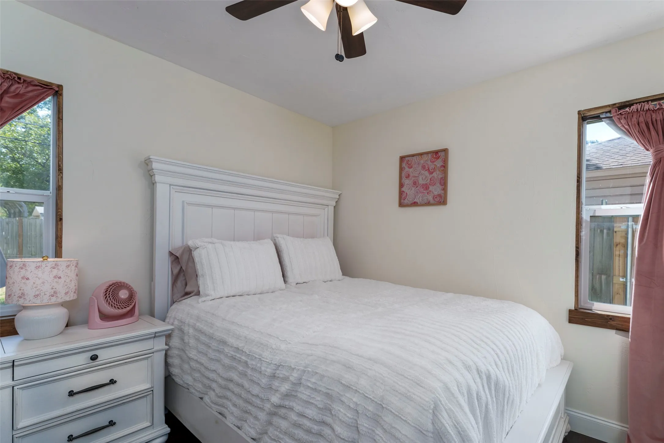 White paneled headboard with decorative molding, ceiling fan with integrated lighting, and two windows with wood-finish trim