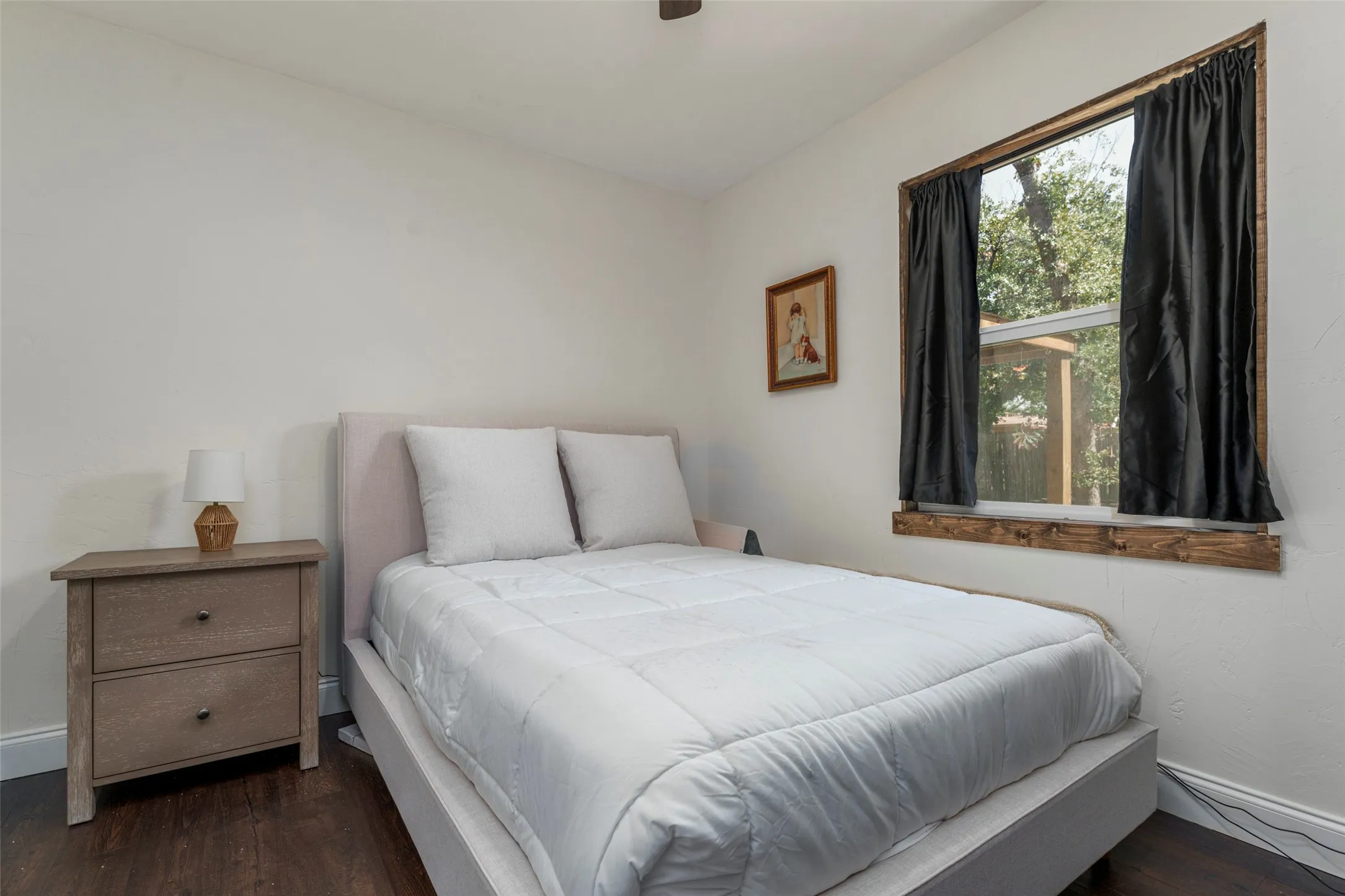 Wood-finish flooring, white painted walls, and a window with wood-finish trim