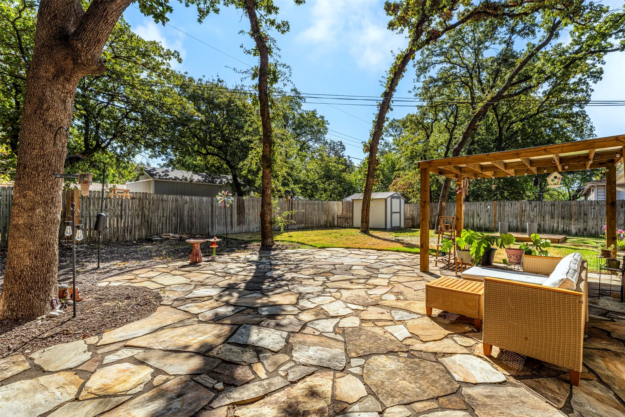 Expansive flagstone patio with a wood pergola, mature trees, wood fence, and a storage shed