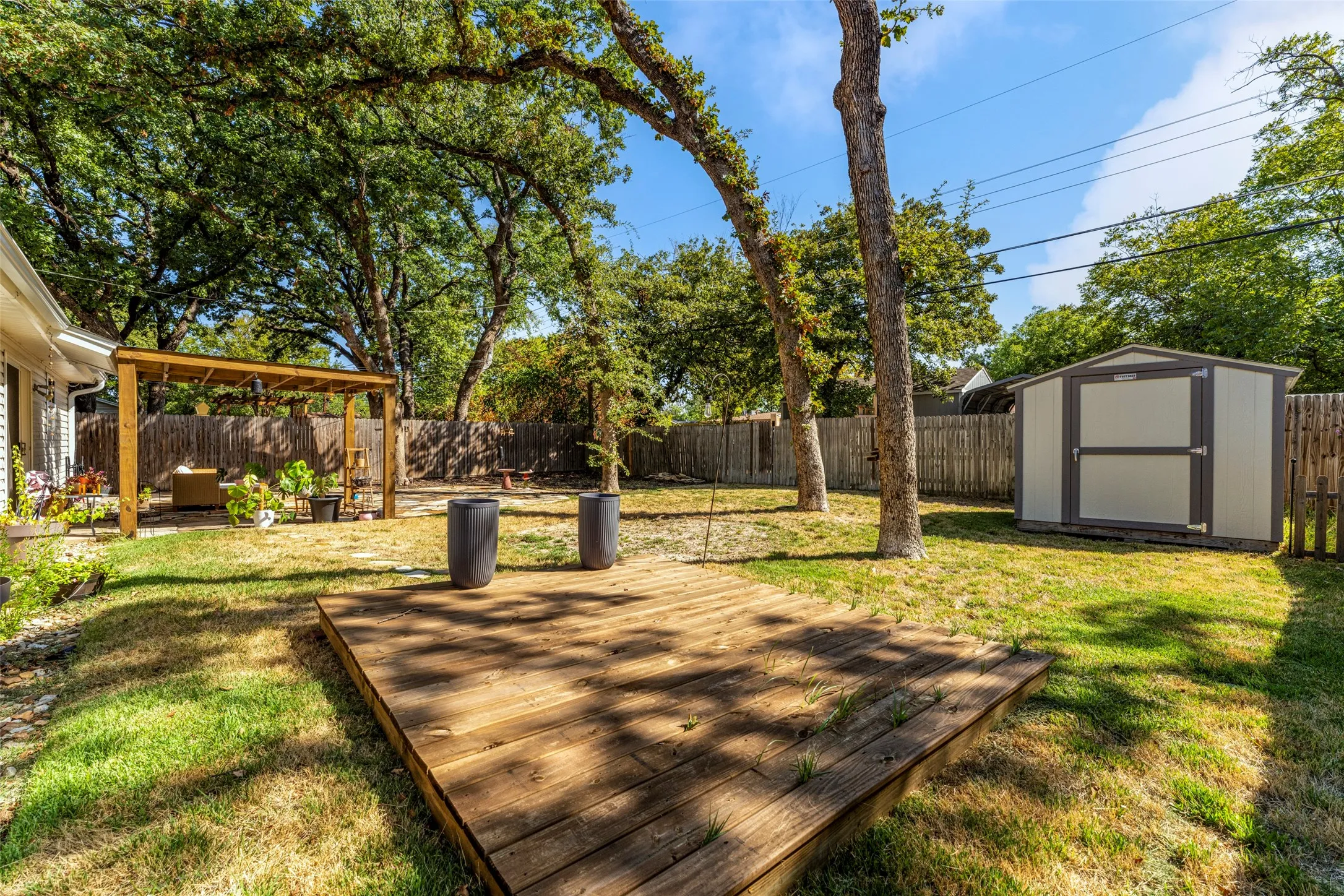 Expansive backyard featuring a wood-finish deck, a coordinating wood-finish pergola, a functional storage shed, and a privacy fence