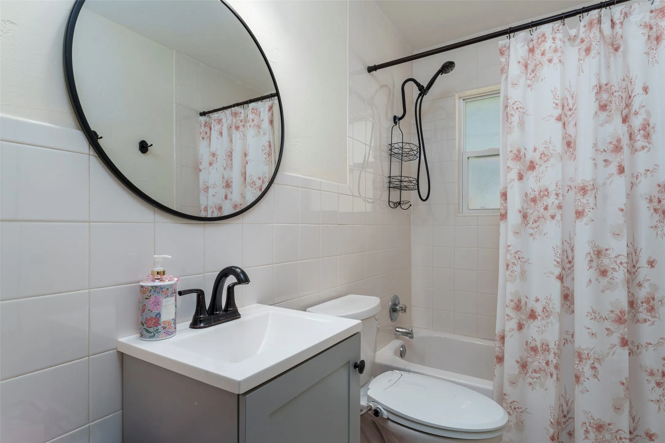 Vanity with black faucet, framed mirror, tiled walls, and bathtub with shower