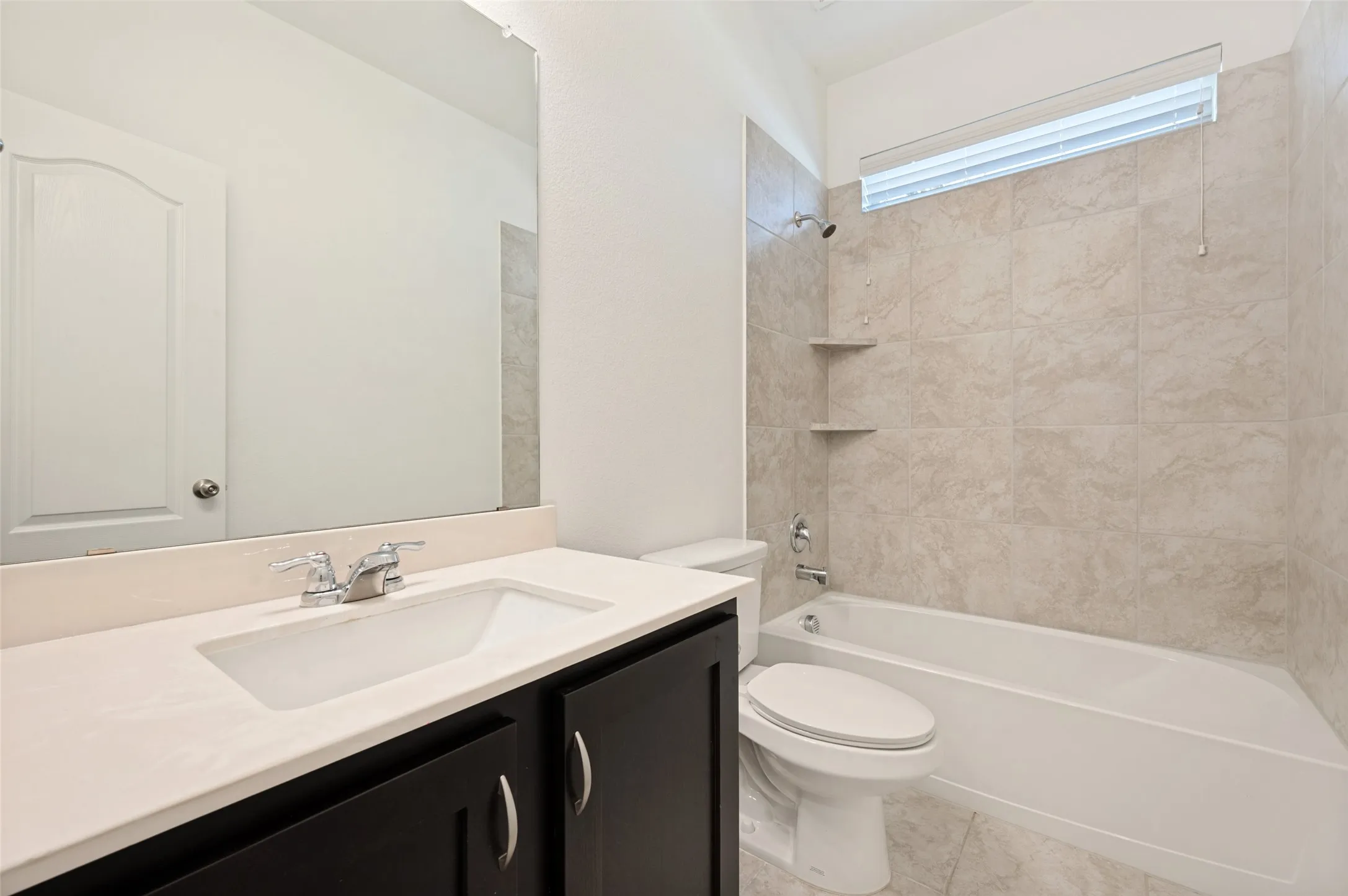 Bathroom featuring a dark wood-finish vanity, integrated sink, chrome faucet, and tiled shower with built-in shelving