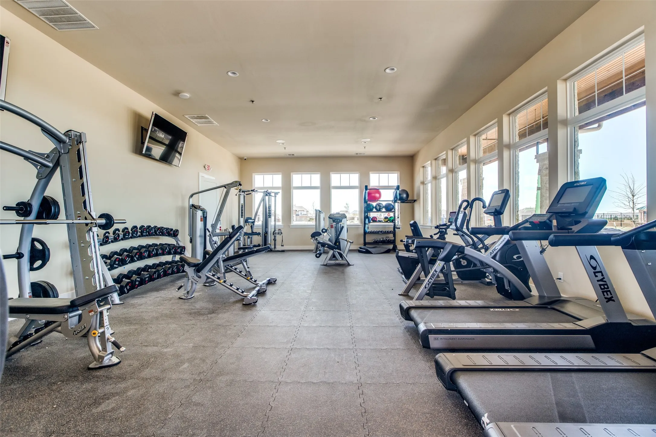 Dedicated fitness room featuring cushioned flooring, multiple window banks, recessed lighting, and wall-mounted televisions