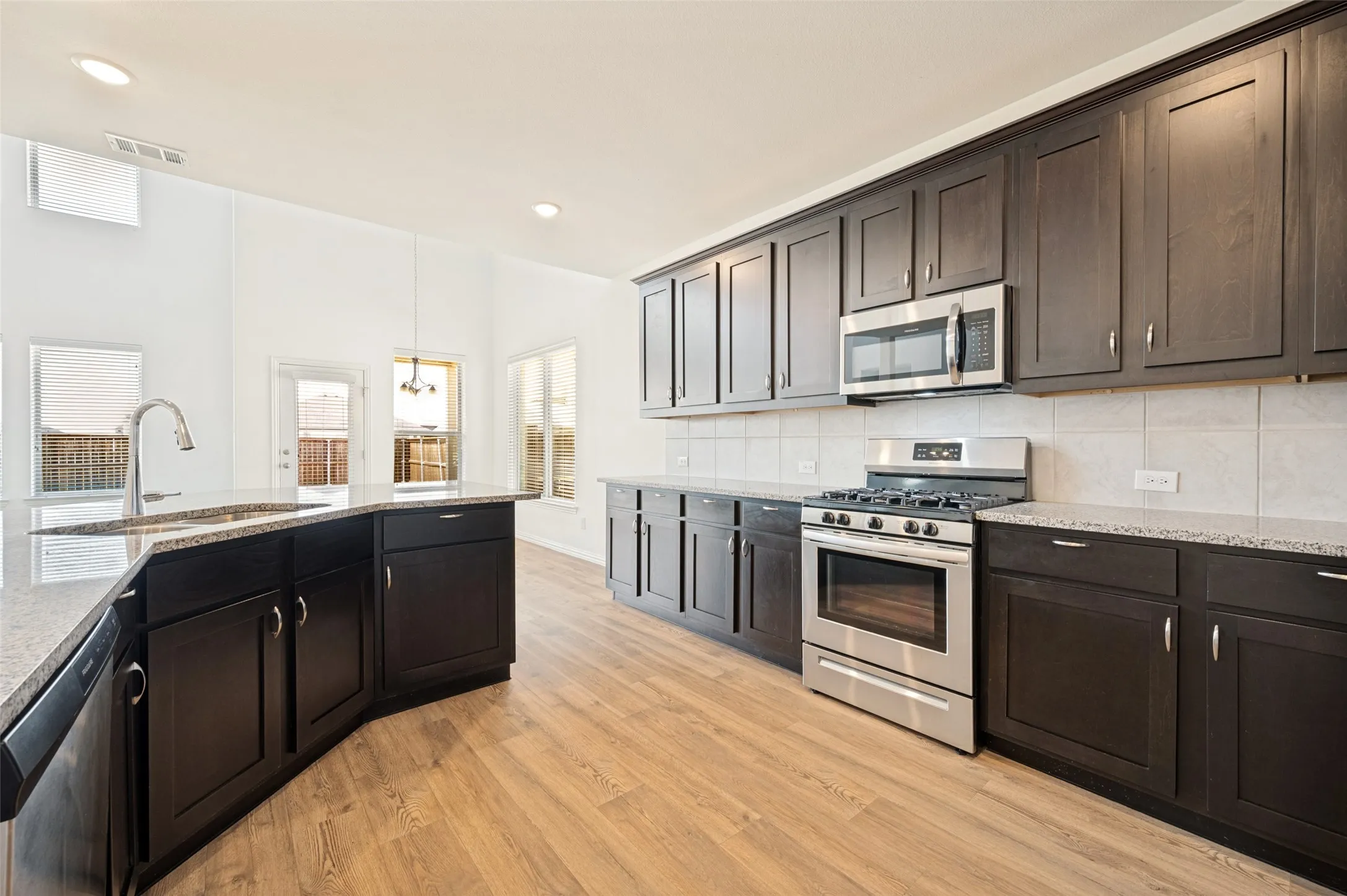 Kitchen featuring dark wood-finish cabinetry, light-toned countertops, stainless steel appliances, and wood-finish flooring