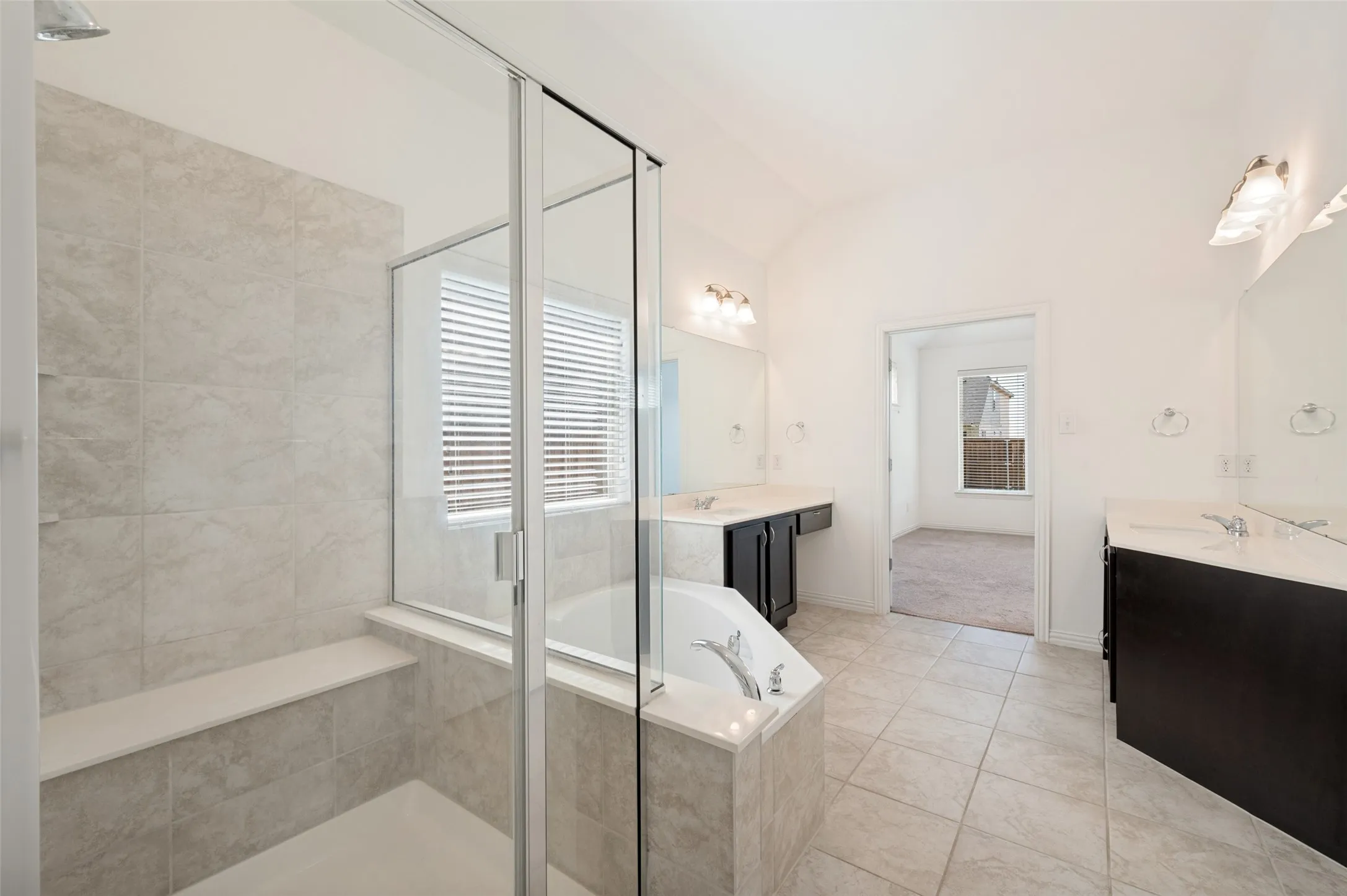 Glass-enclosed shower with a built-in bench, corner soaking tub, and dual vanities with integrated sinks