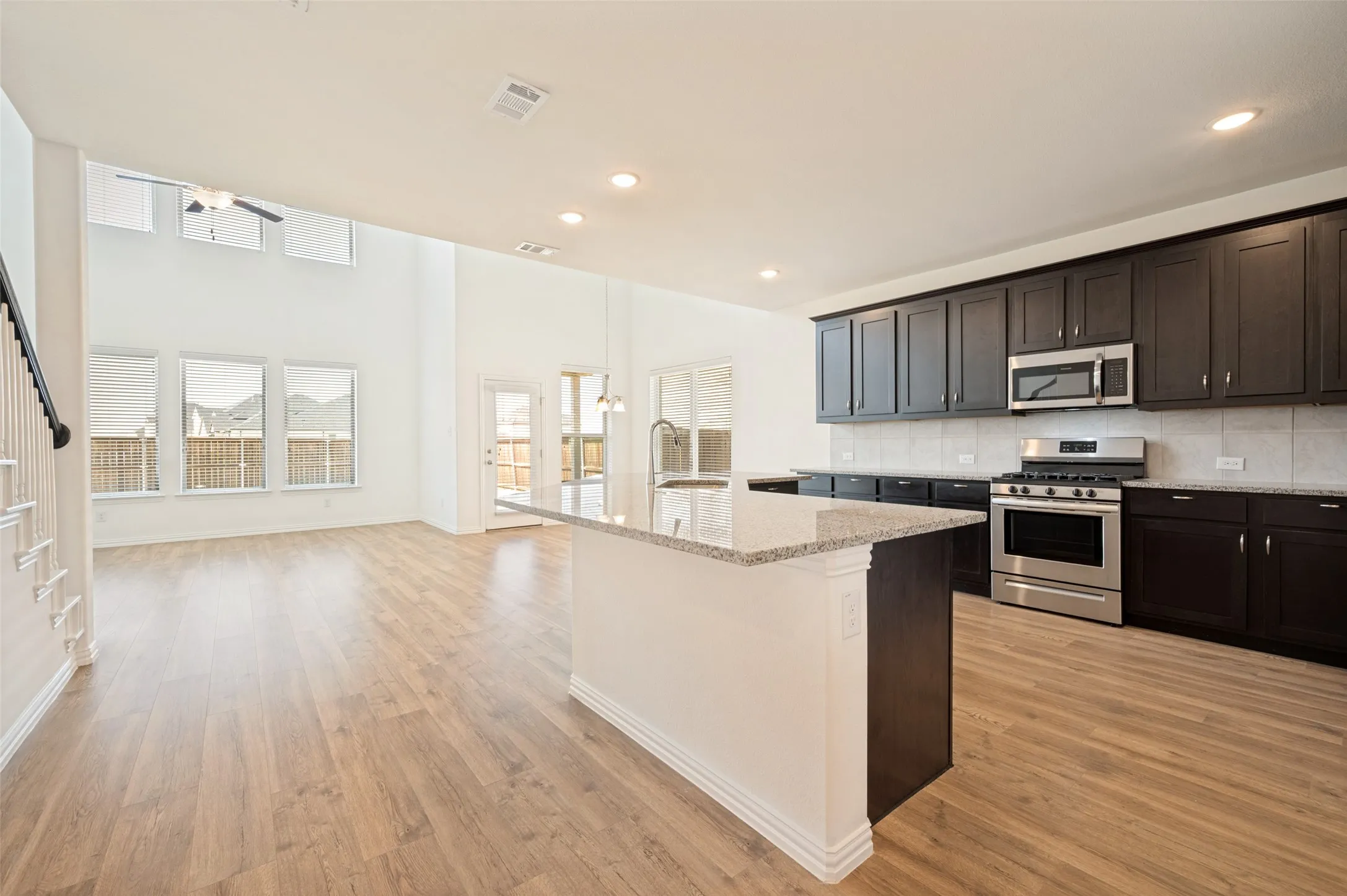 Open-concept kitchen with dark wood cabinetry, stainless steel appliances, and a granite-topped island