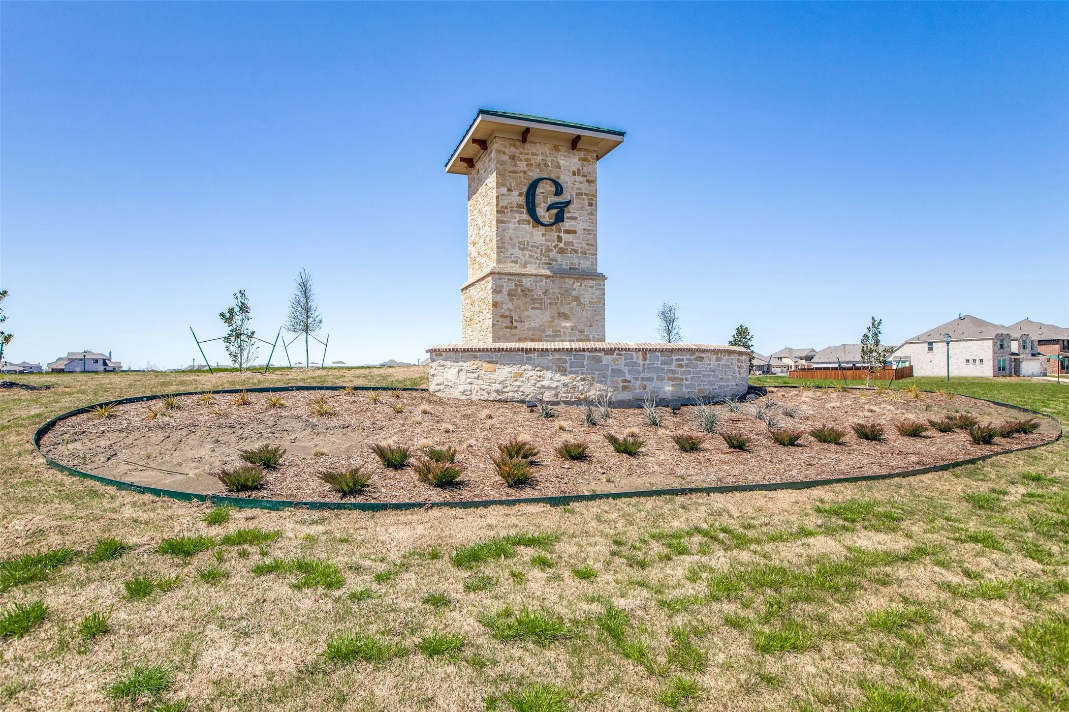 Stone and brick community entrance monument with a distinct "G" emblem