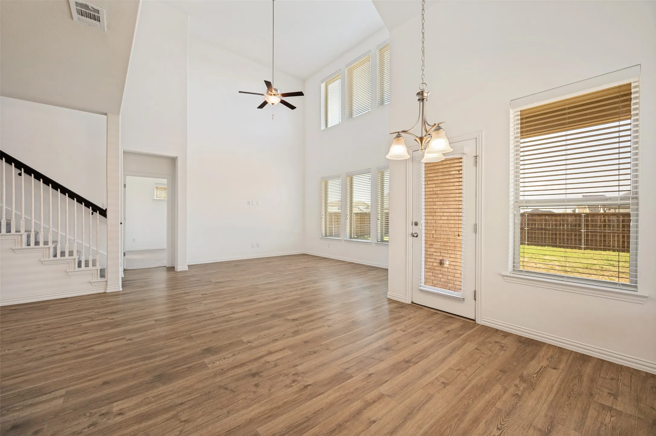 Vaulted ceilings, wood-finish flooring, staircase with white spindles, multiple windows, and a glass-paneled door