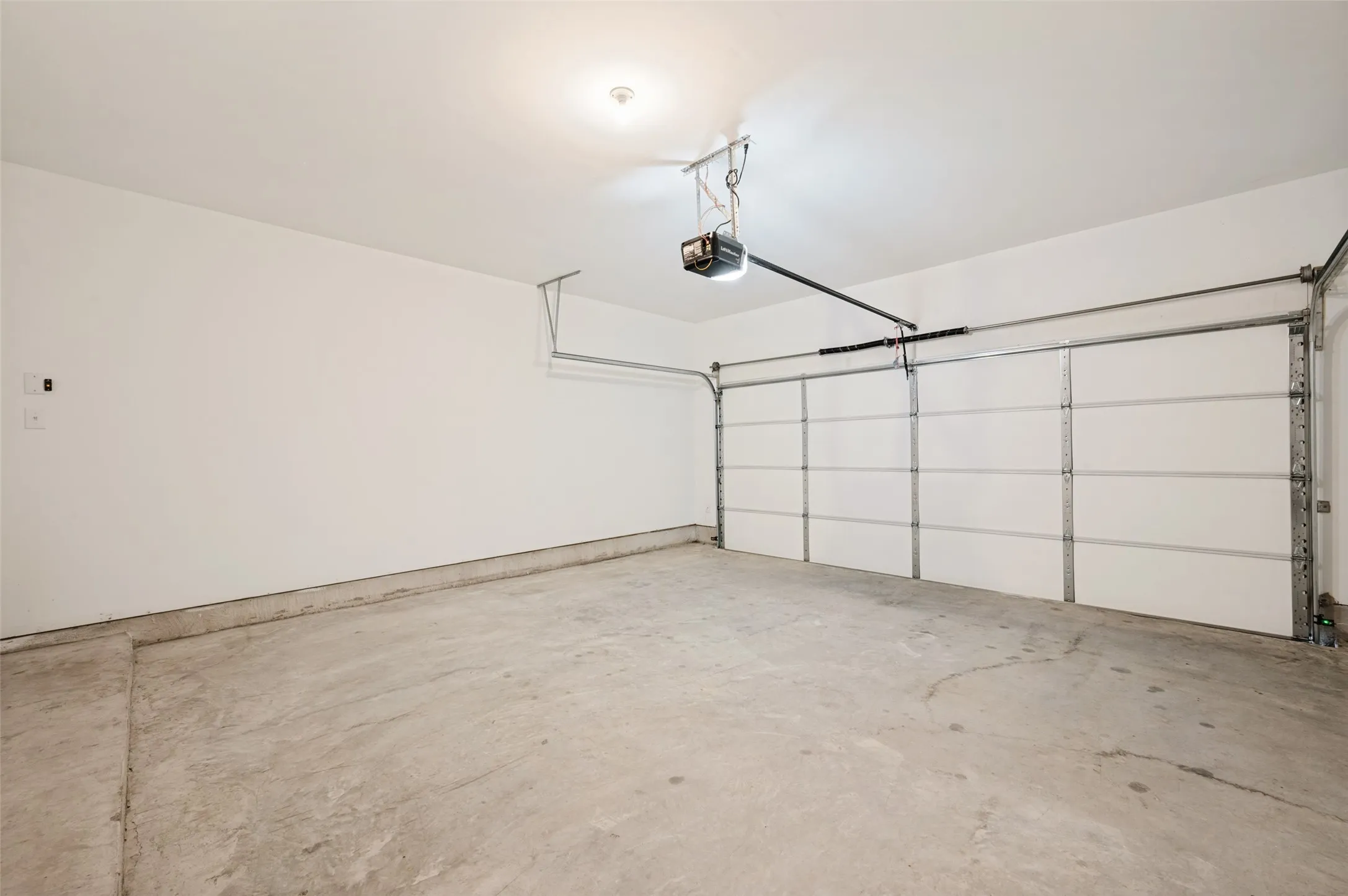Spacious garage with concrete flooring, white walls, and an automatic garage door opener