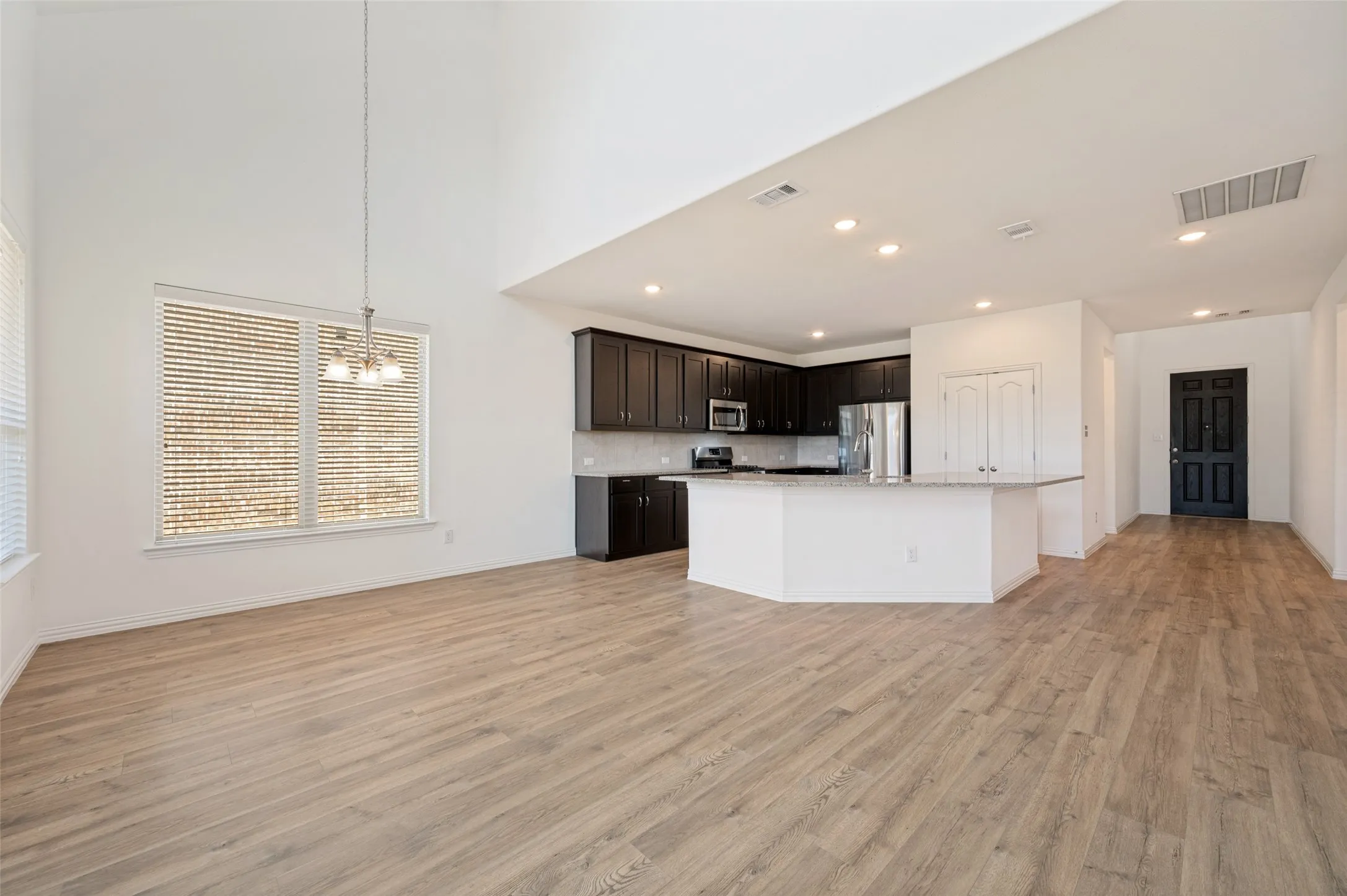 Open-concept living space featuring high ceilings, wood-finish flooring, a kitchen island with stone countertops, and dark wood cabinetry