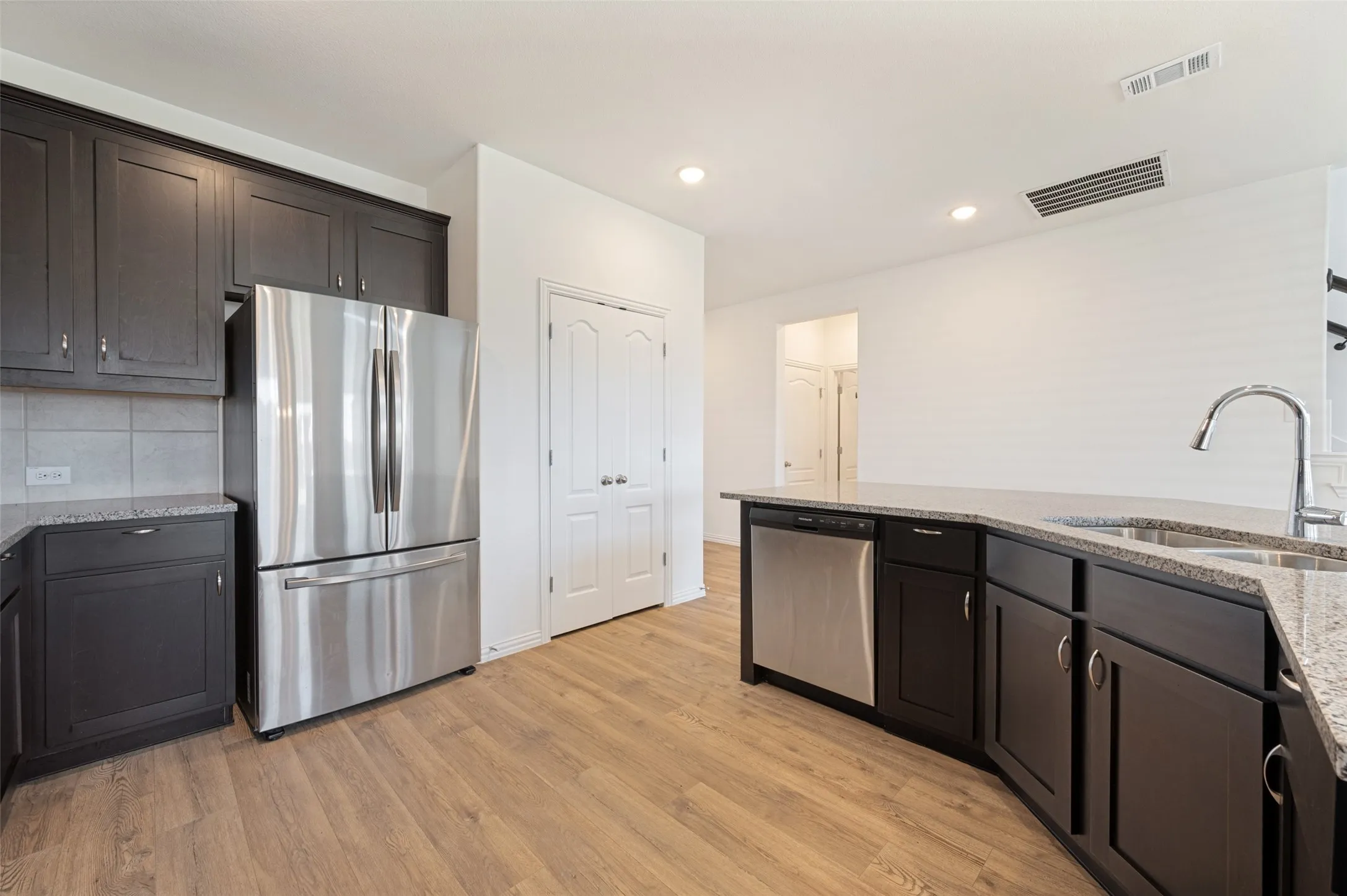 Wood-finish flooring throughout, dark cabinetry, stainless steel appliances, recessed ceiling lighting, and a kitchen island with an undermount sink