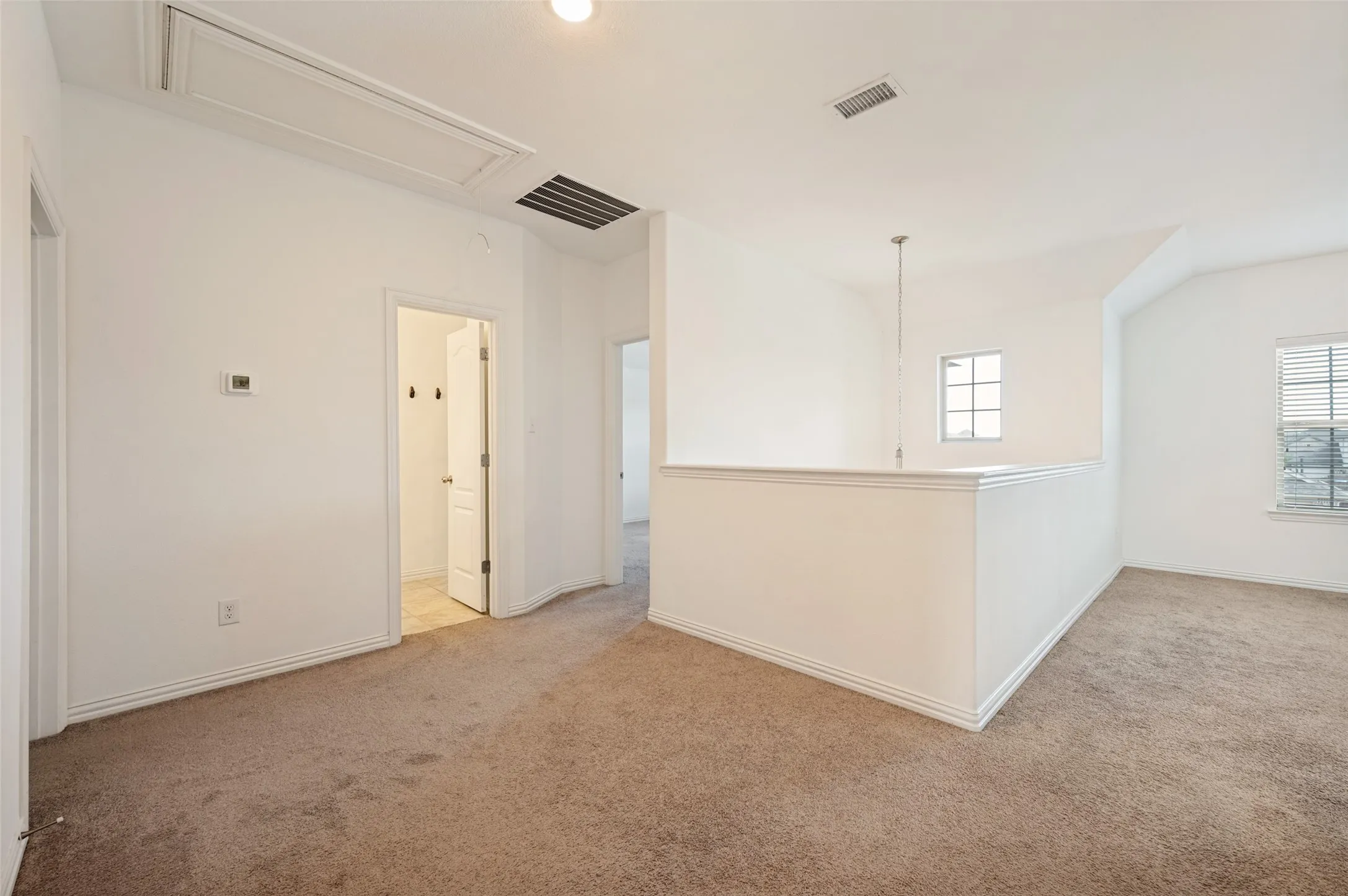 Carpeted loft area featuring a half-wall partition, two windows, and overhead lighting