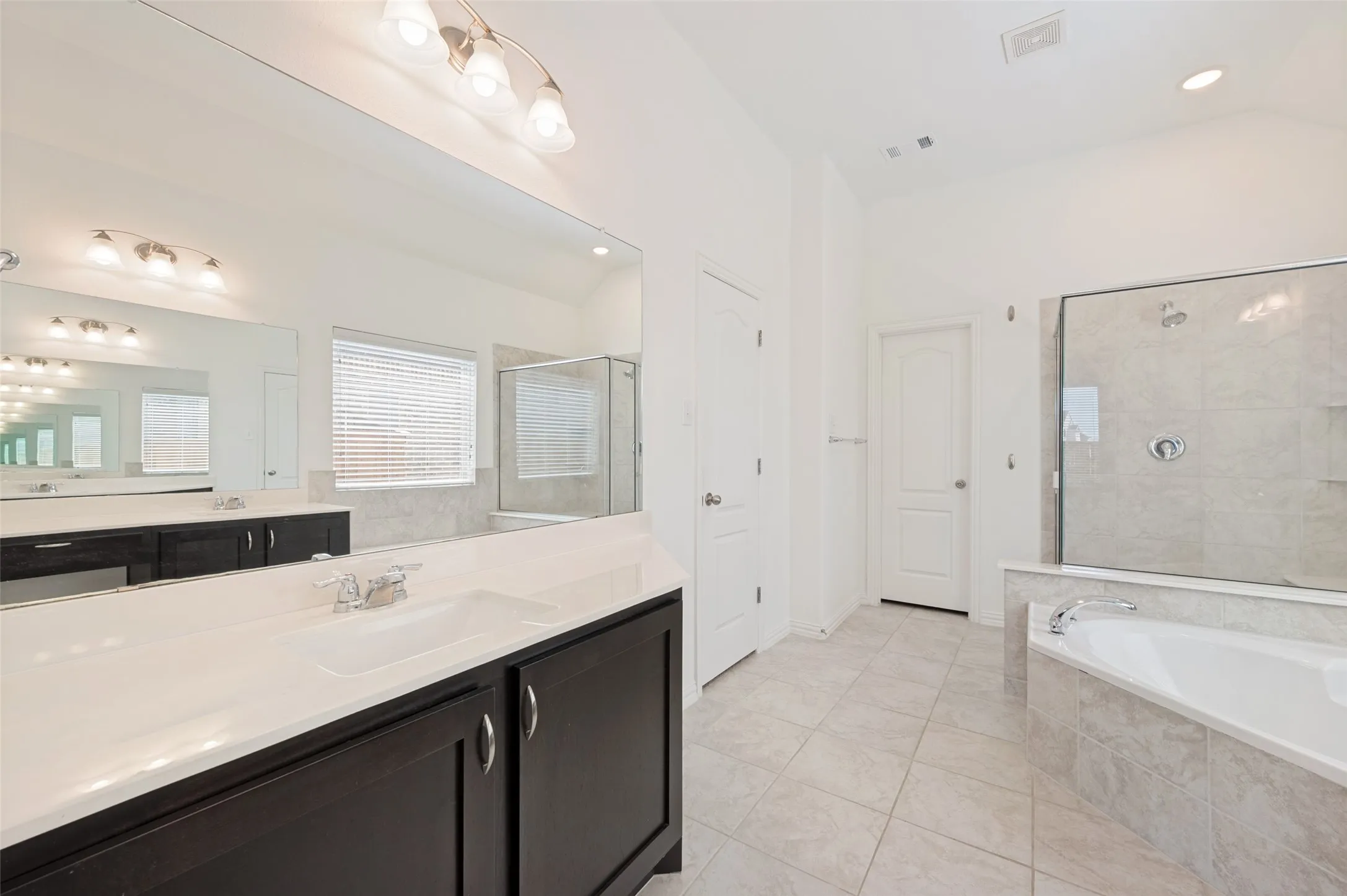 Dual vanity with dark wood-finish cabinetry, integrated sinks, and a large wall-mounted mirror