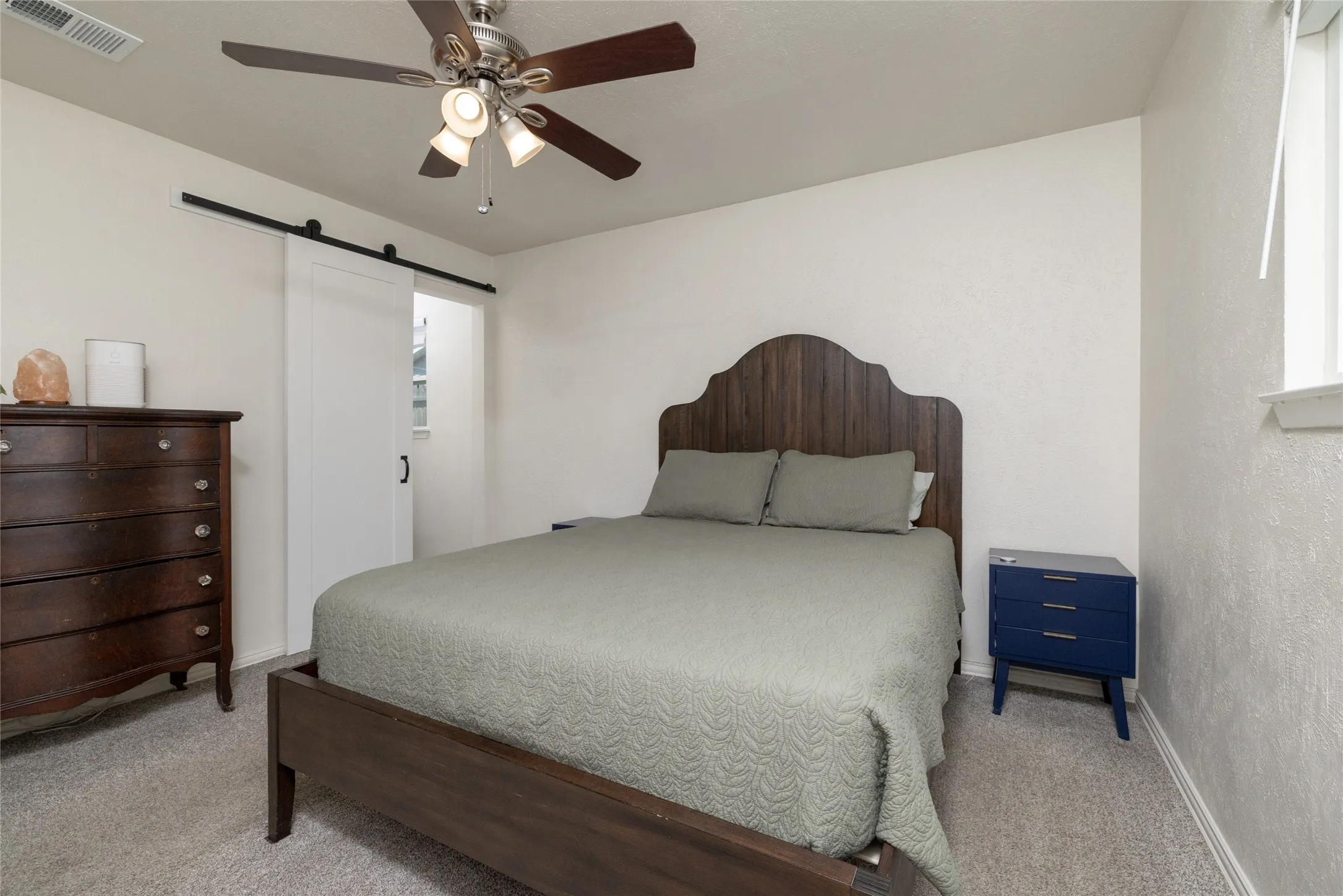 Carpeted room featuring a ceiling fan with integrated lighting, a barn door, and a single window with blinds