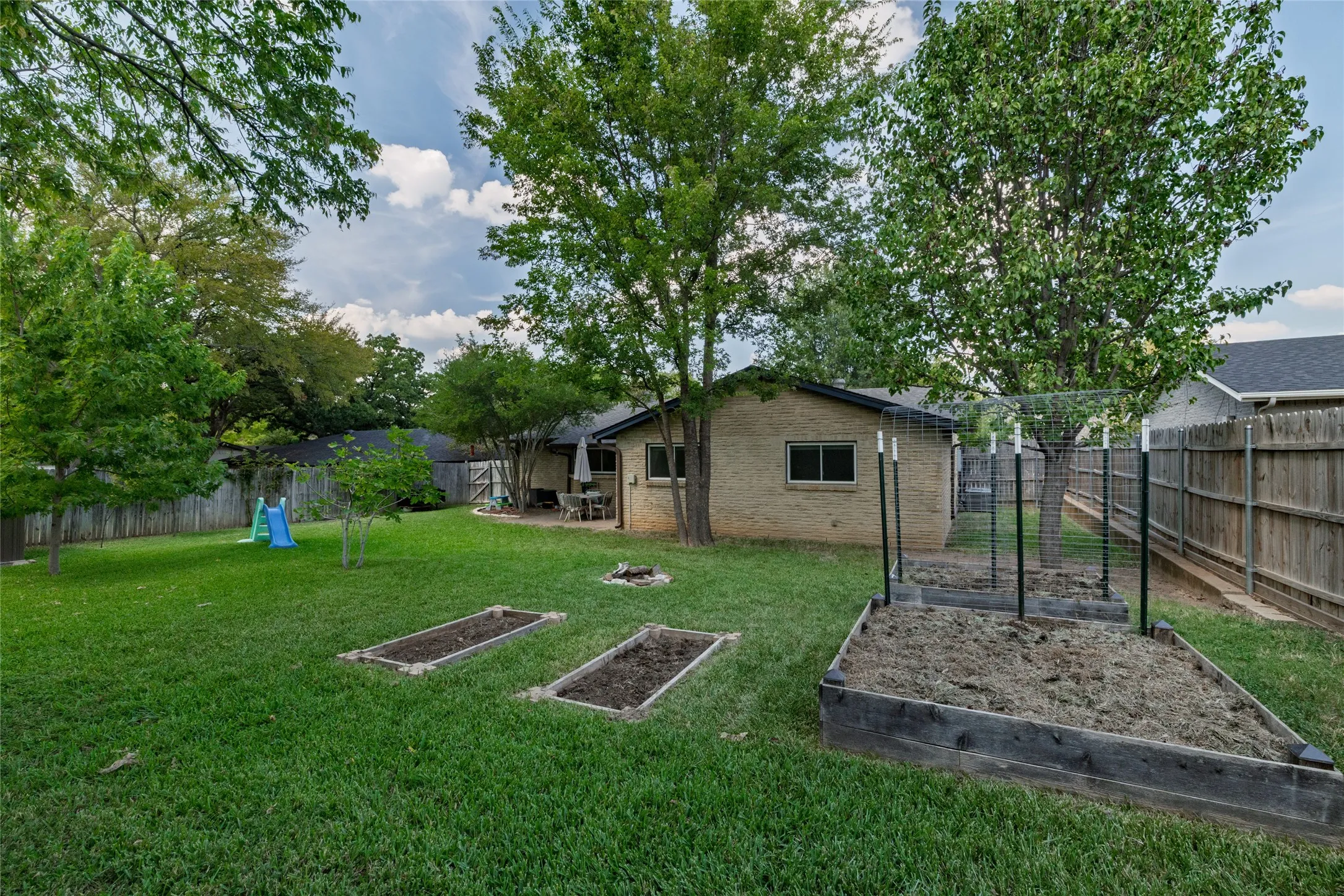 Expansive backyard featuring a manicured lawn, established trees, a brick exterior, and raised garden beds