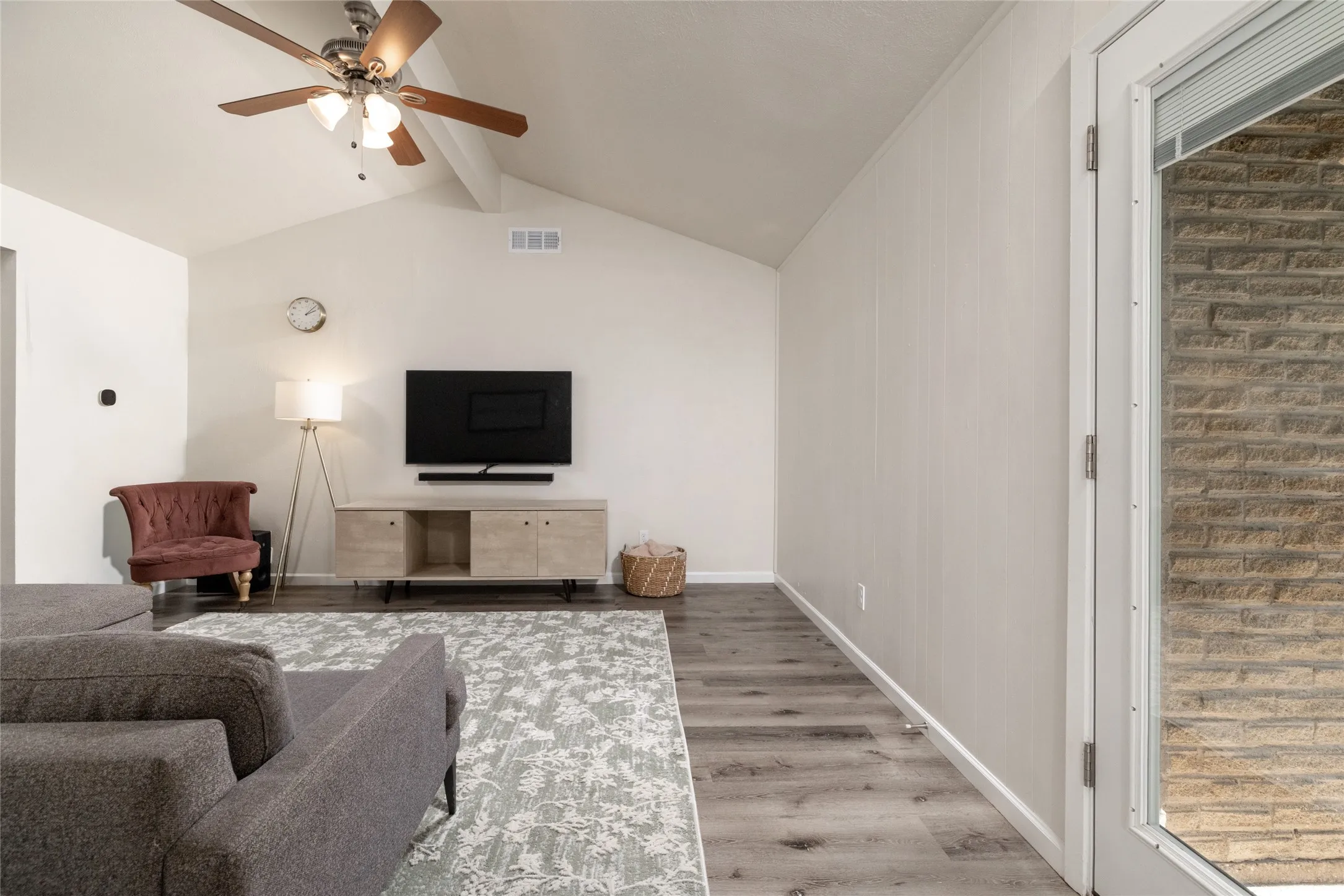 Vaulted ceilings, wood-finish flooring, ceiling fan with integrated lighting, glass-paneled exterior door, and light-toned interior walls