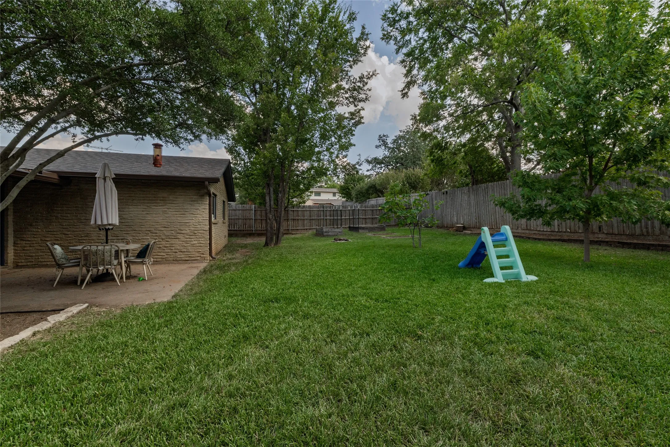 Expansive backyard featuring a lush lawn, mature trees, and a privacy fence