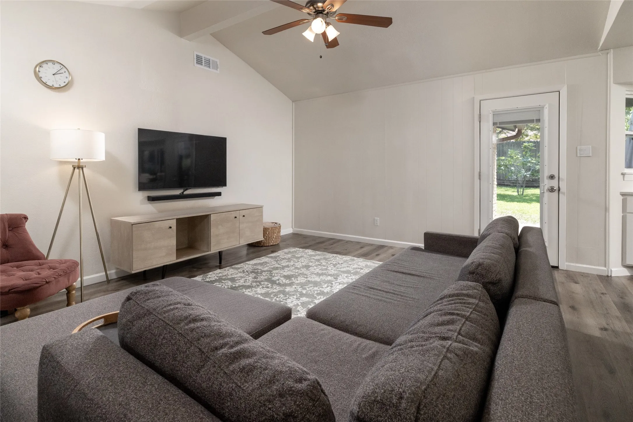 Vaulted ceiling with a ceiling fan, wood-finish flooring, and a rear exterior door with a glass panel