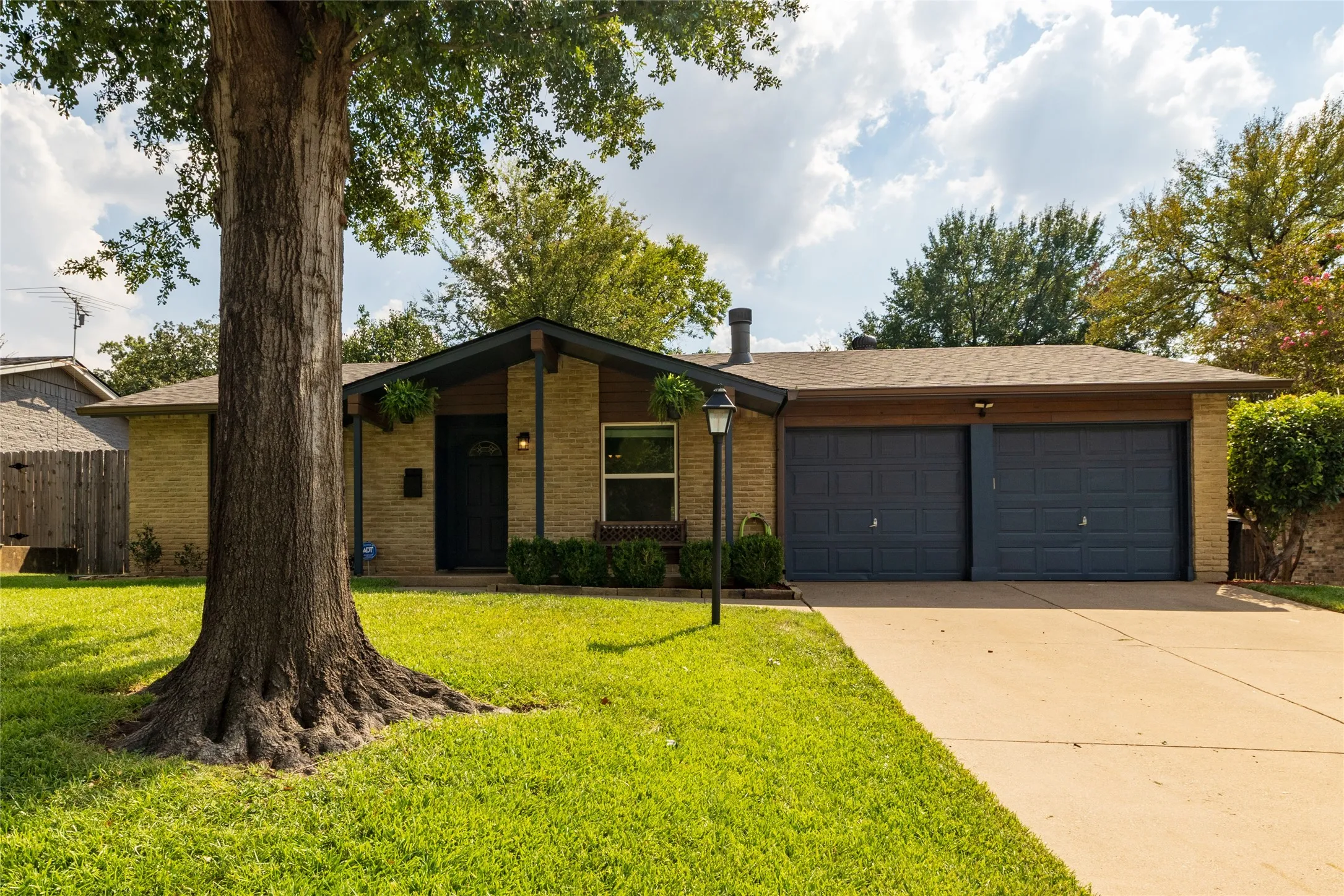 Brick exterior with gabled entry, dual garage doors, concrete driveway, and established landscaping