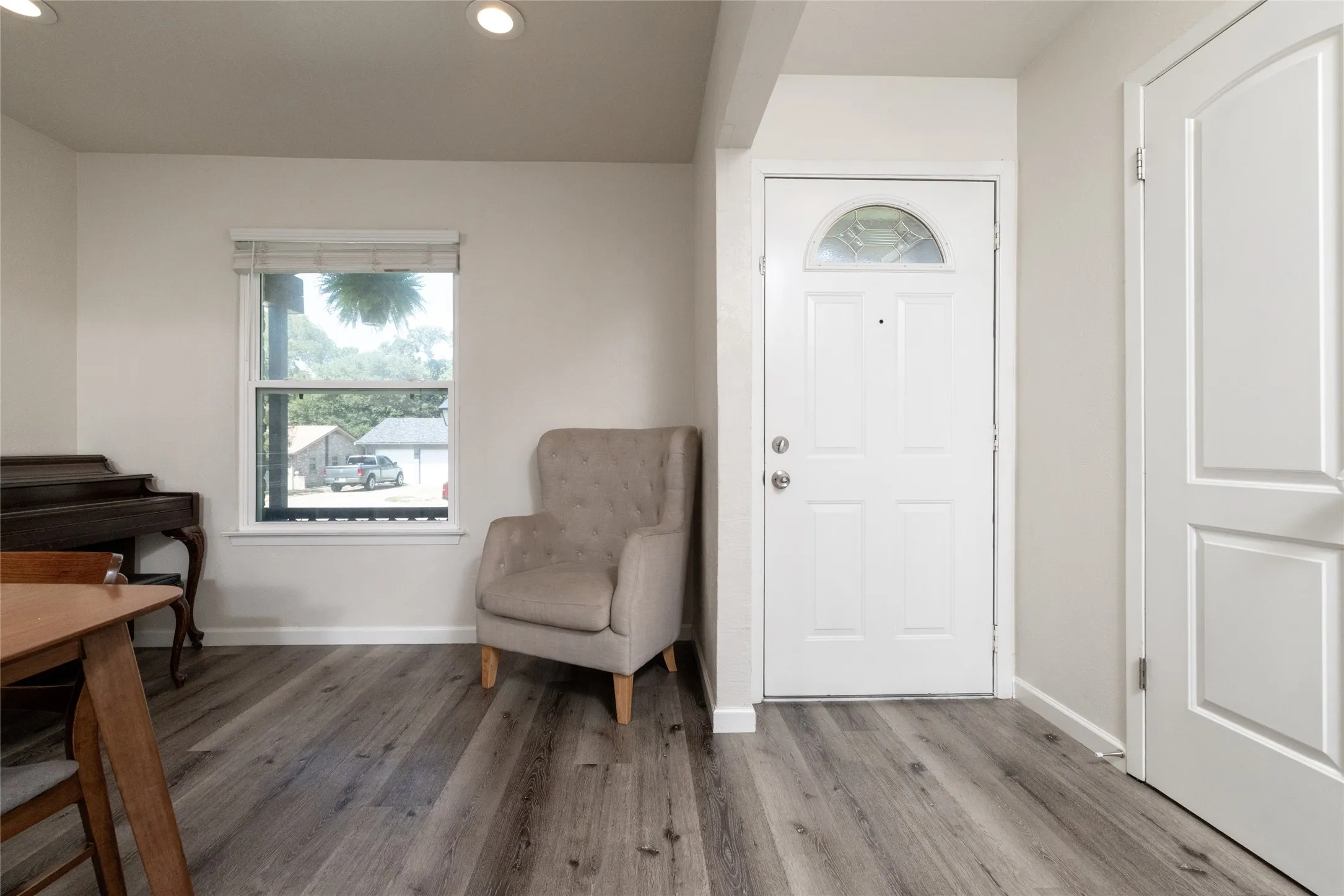 Wood-finish flooring throughout, white entryway door with decorative glass, recessed ceiling lighting, and a single-pane window